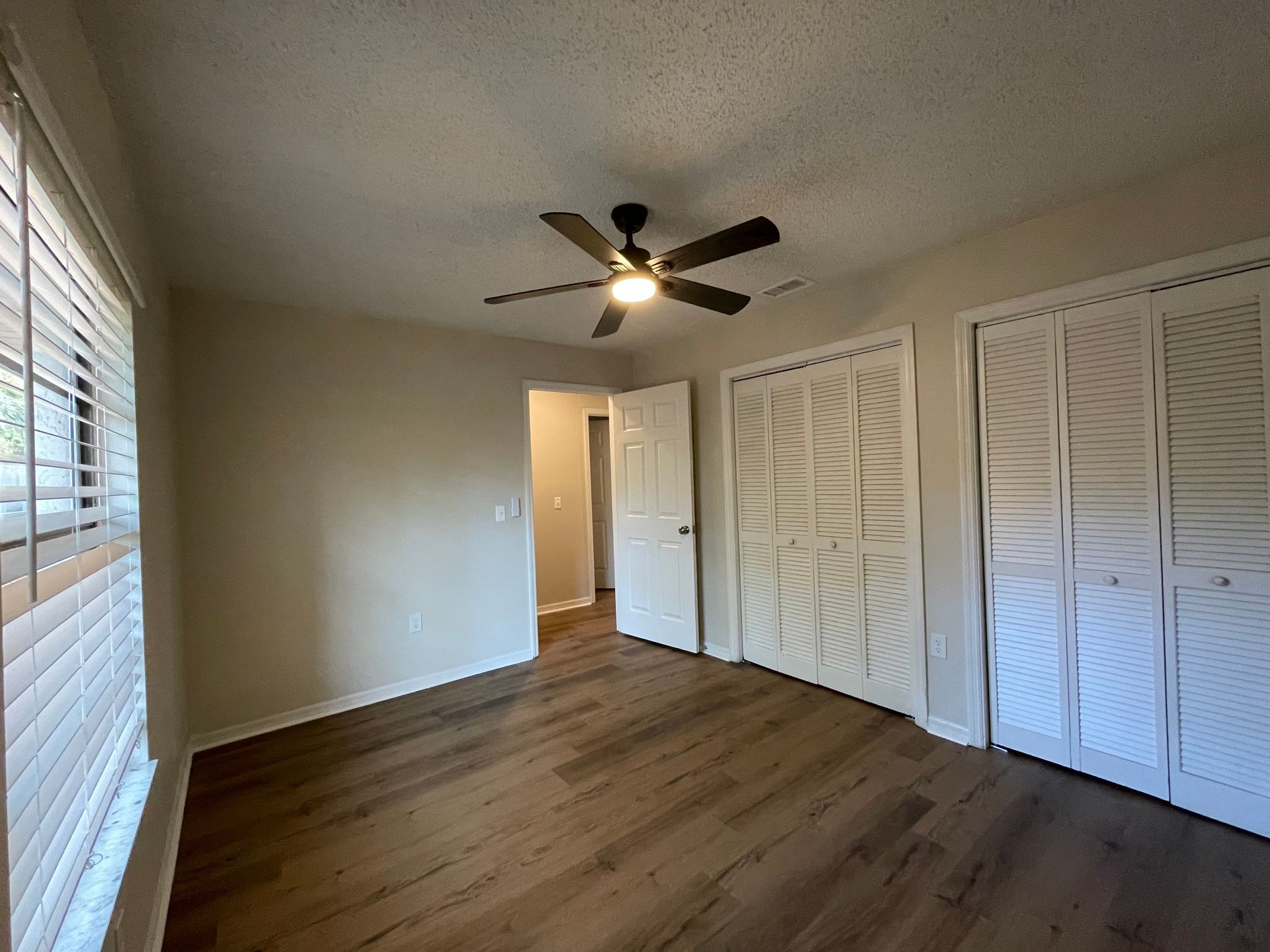 An empty bedroom with hardwood floors and a ceiling fan.