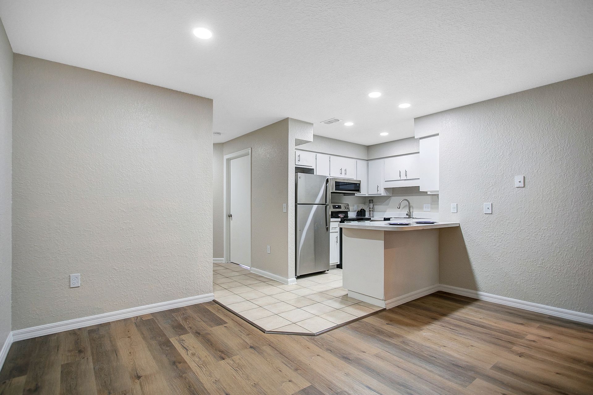 A living room with hardwood floors and a kitchen in the background.