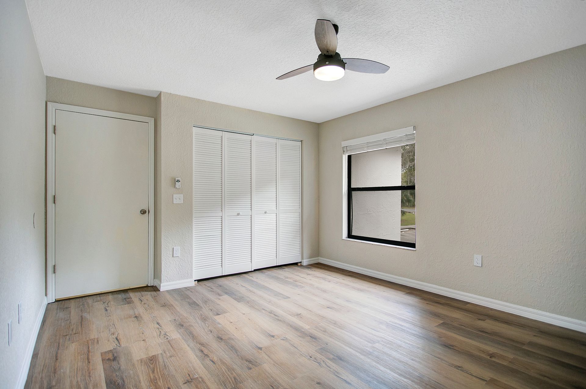 An empty bedroom with hardwood floors and a ceiling fan.