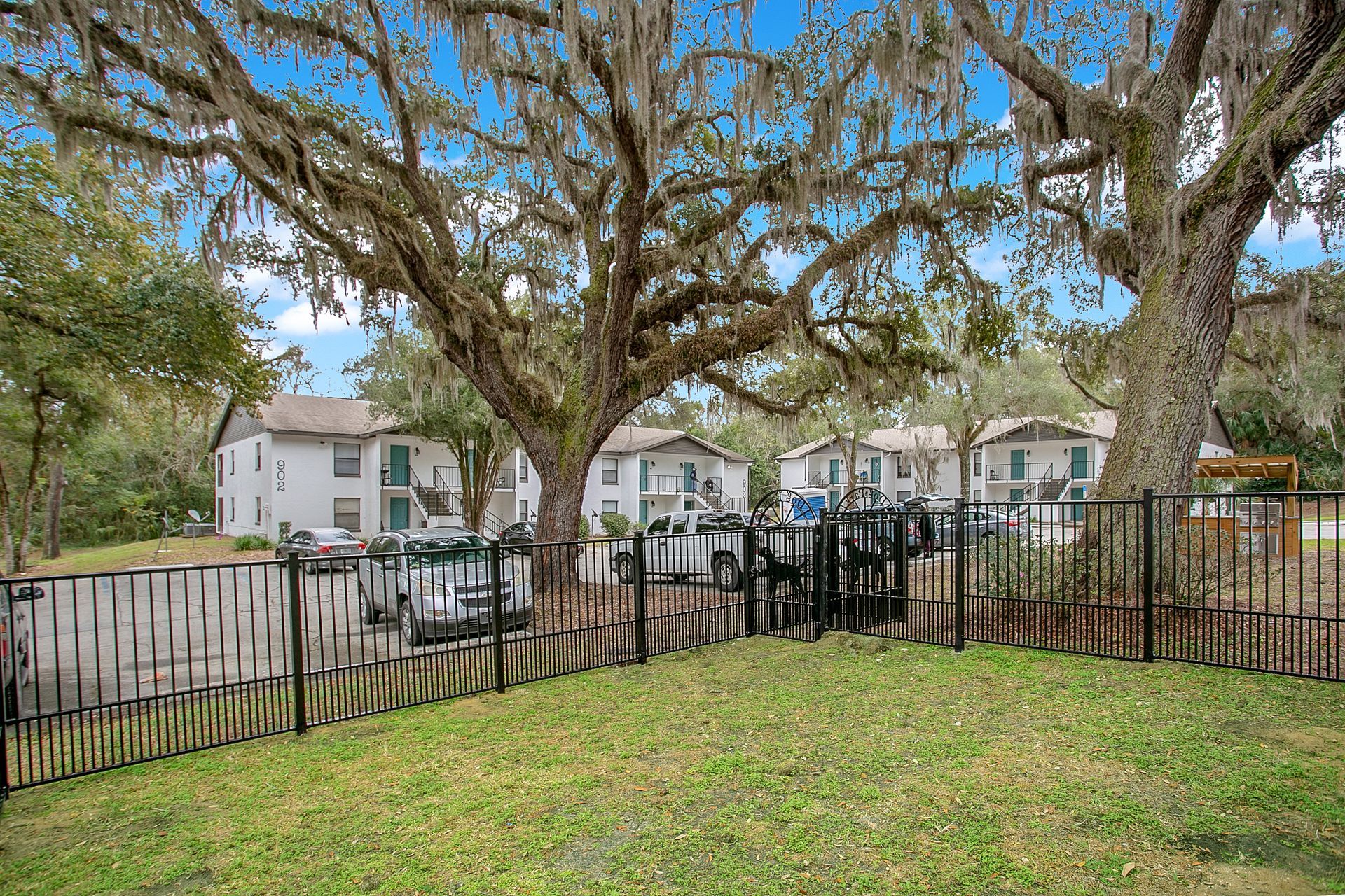 A fence surrounds a park with trees and houses in the background.