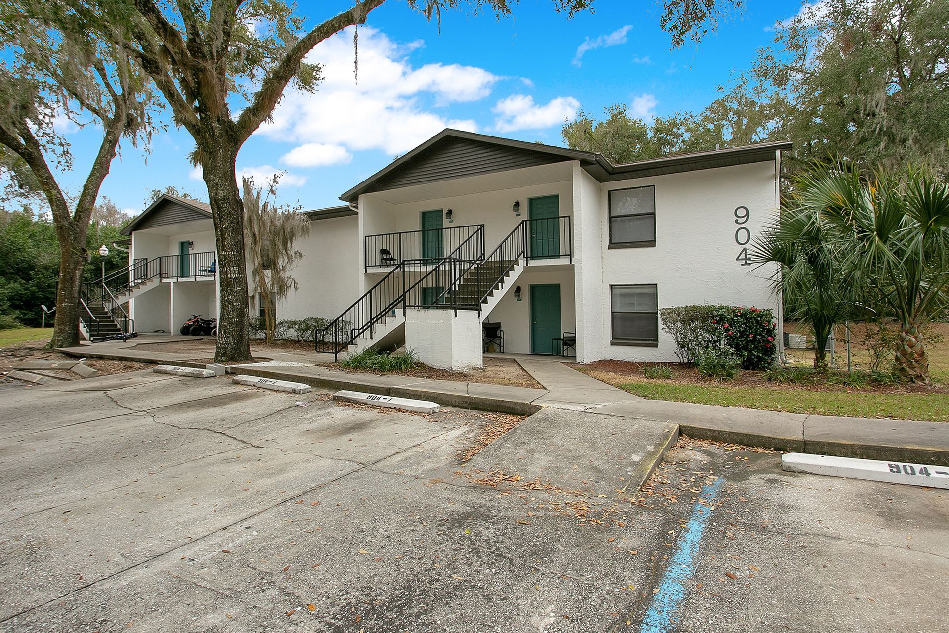 A white apartment building with stairs and a parking lot in front of it.