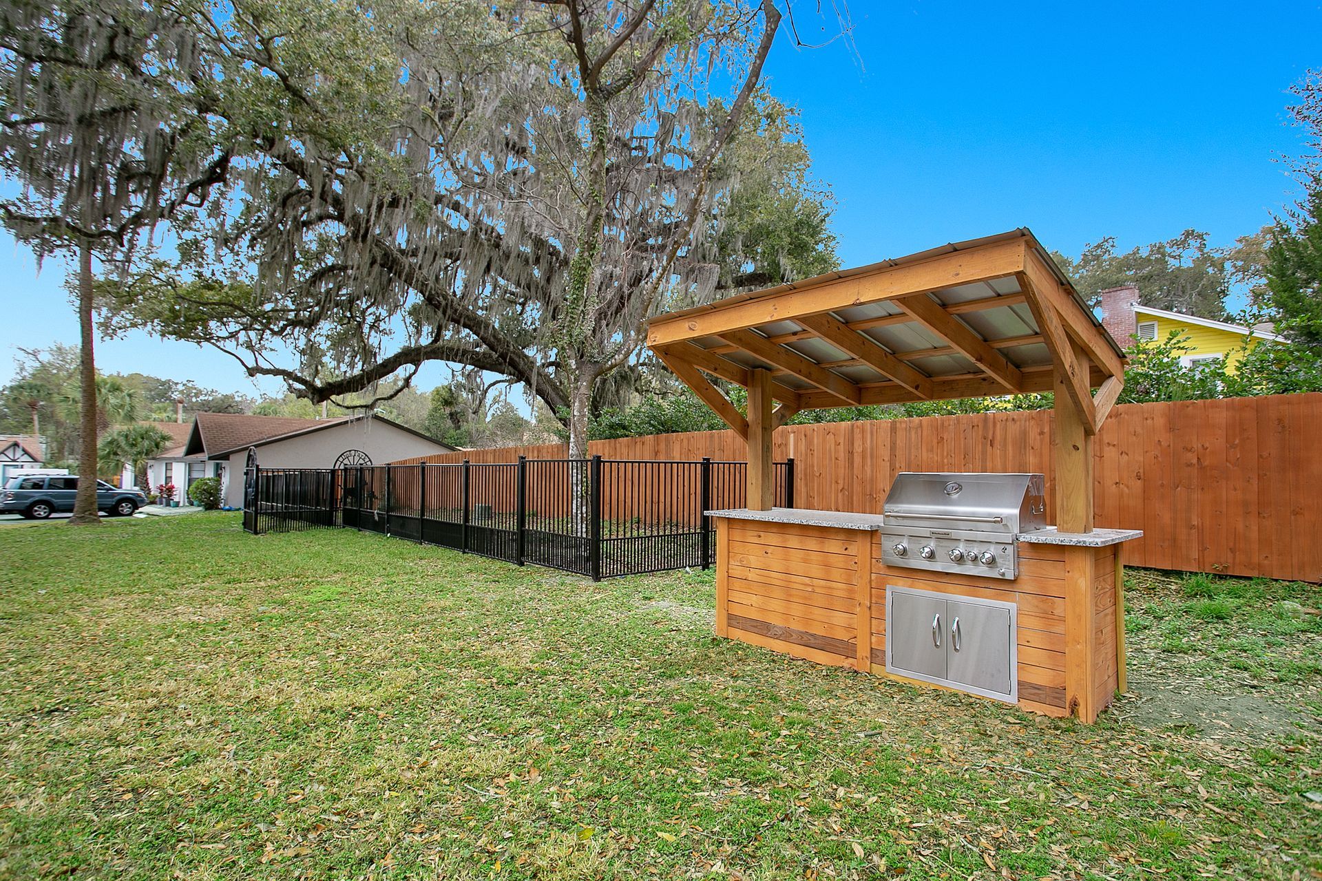 A grill is sitting under a wooden structure in the backyard of an apartment building.