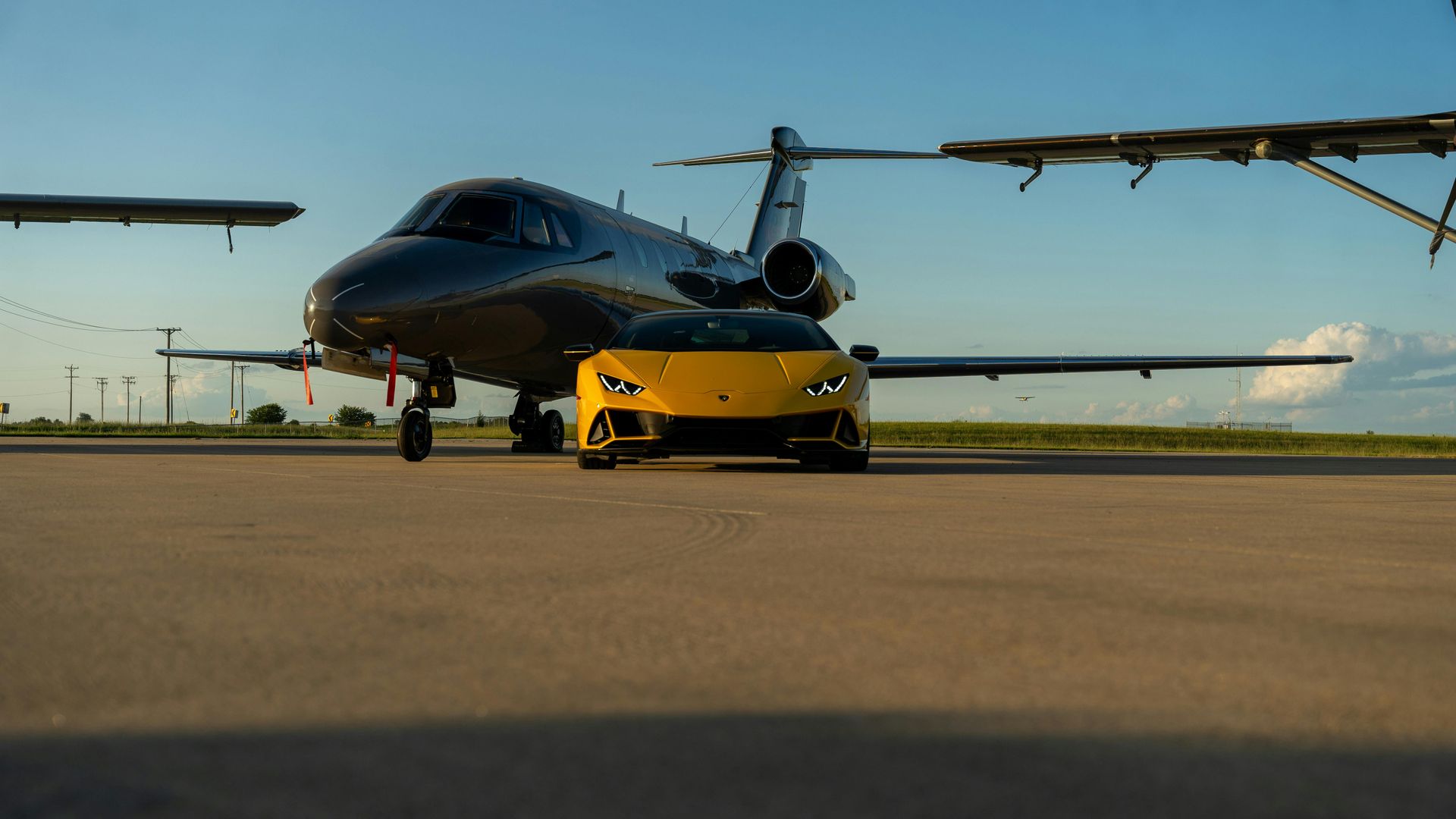 A yellow sports car is parked next to a private jet on a runway.