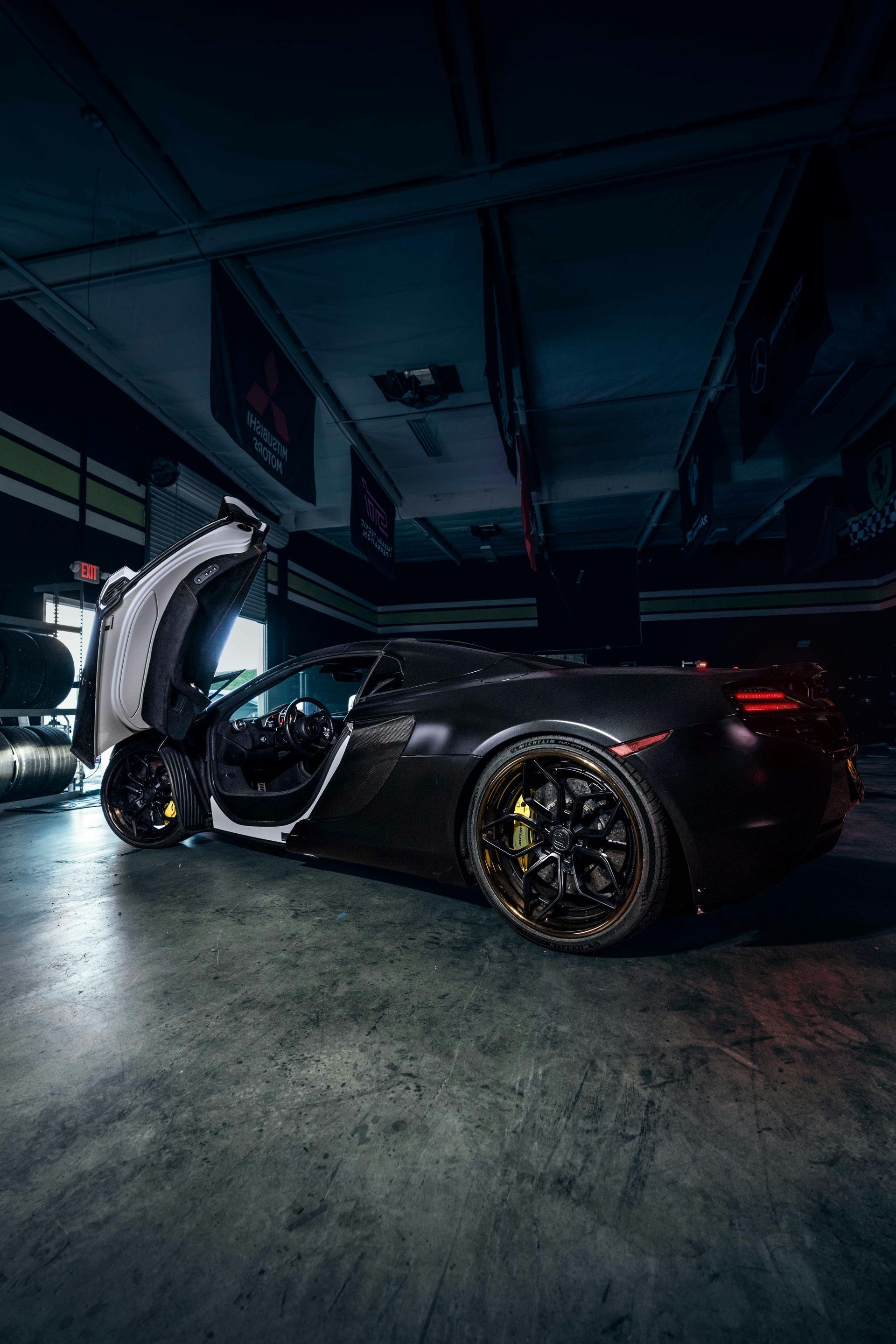 A black sports car is parked in a garage with its doors open.