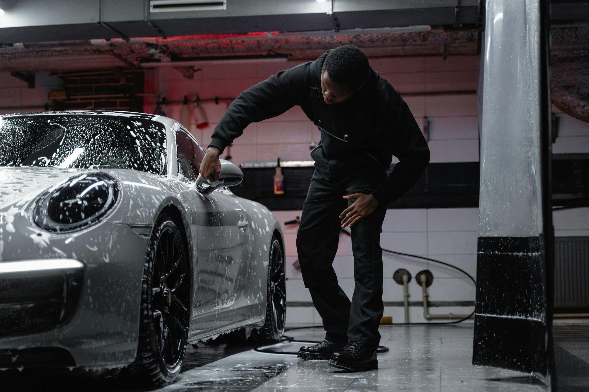 A man is washing a silver sports car in a garage.