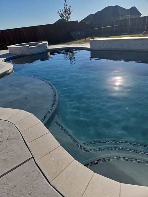 Pool with blue water and stone steps. A fire pit and home are in the background.