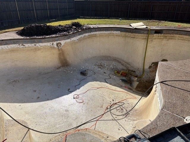 Empty swimming pool under construction; tan walls, concrete floor, tools visible, backyard setting.