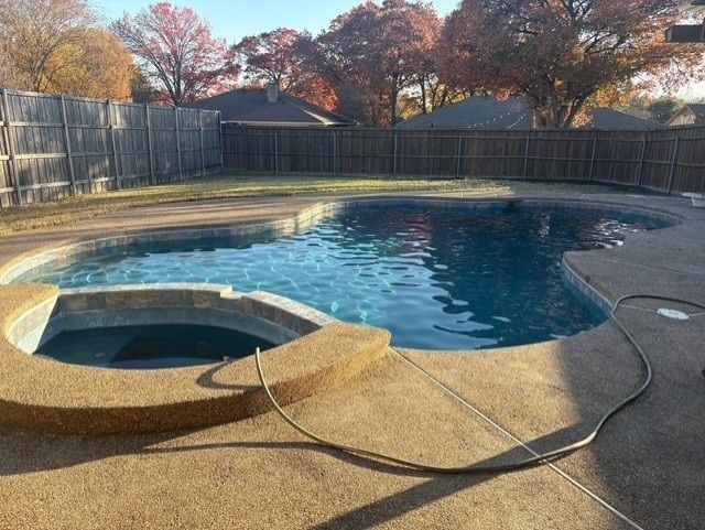 Swimming pool with attached spa in a backyard; water is blue, surrounded by concrete.