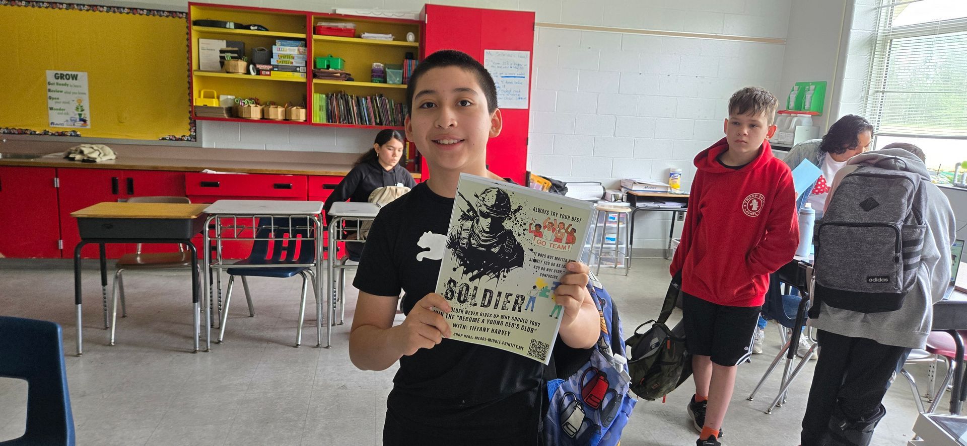 Student holding a certificate in a classroom, with other students in the background