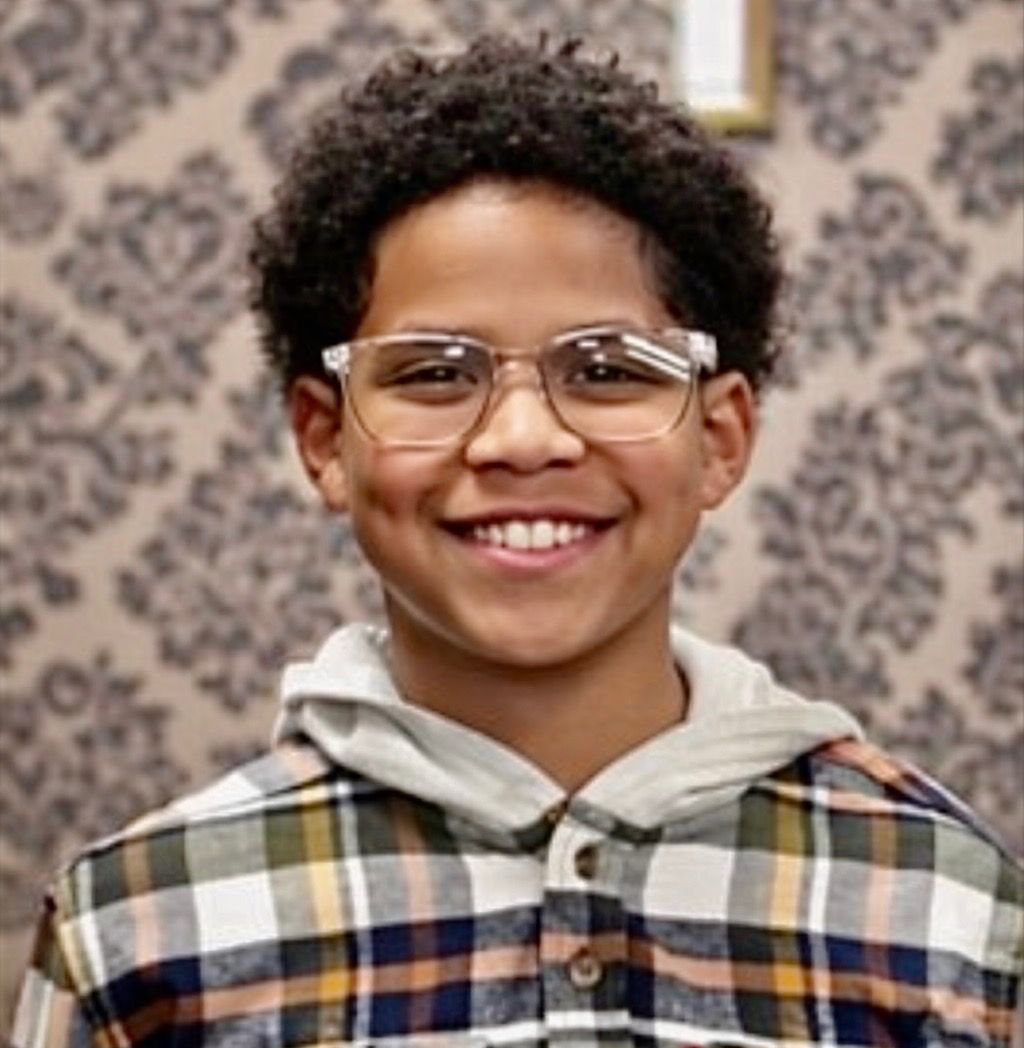 Kaleb person wearing glasses and a plaid shirt against a patterned backdrop
