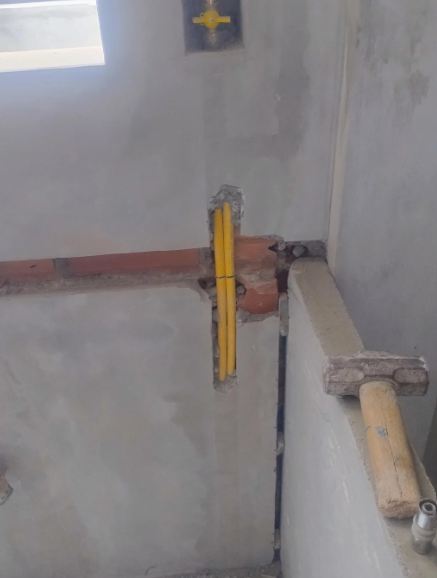 Obra con cableado eléctrico en conducto amarillo, parcialmente incrustado en un muro de ladrillo