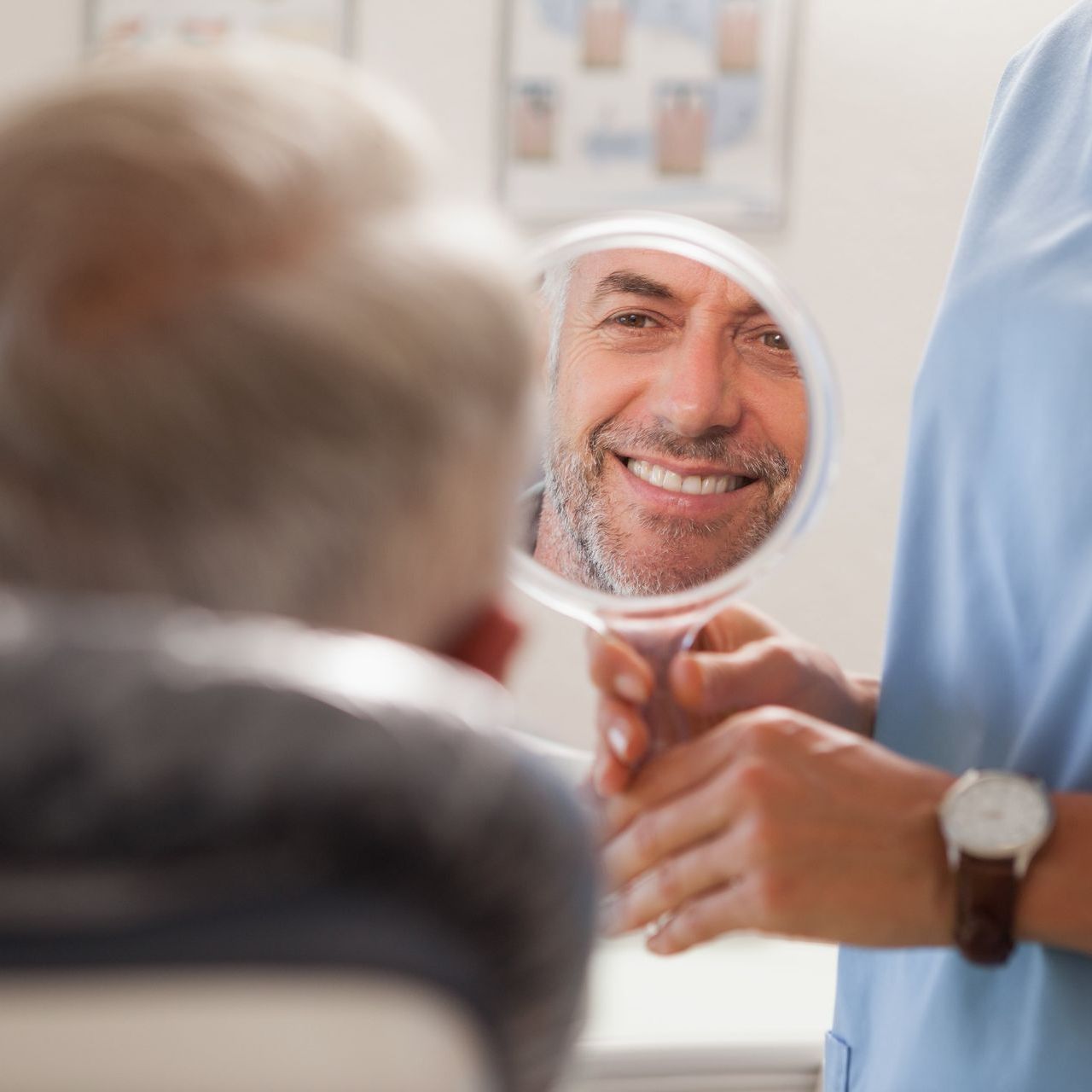 An image of a middle aged man in a dental office smiling while looking at his reflecting in a mirror