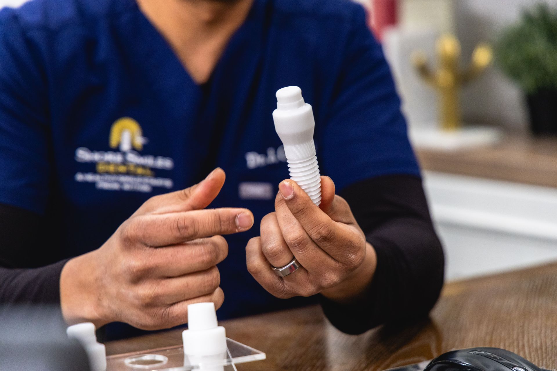 An image of Dr. Gandhi holding a dental implant model