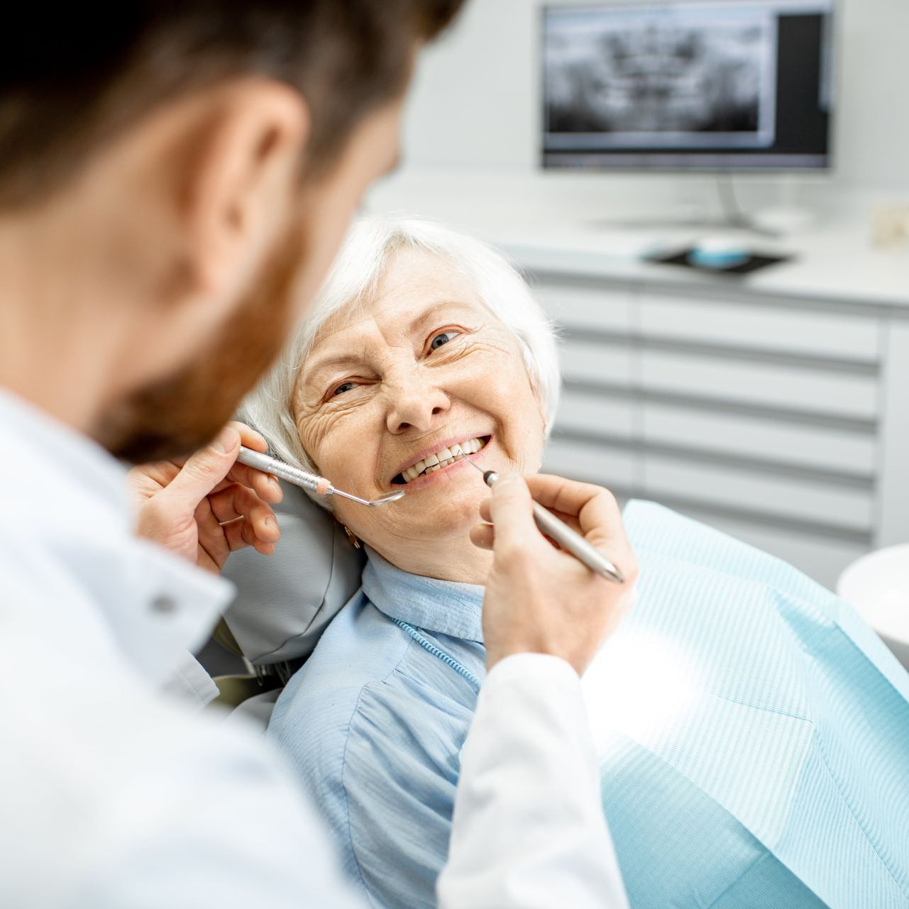 An elderly woman in a dental office smiling at a male dentist