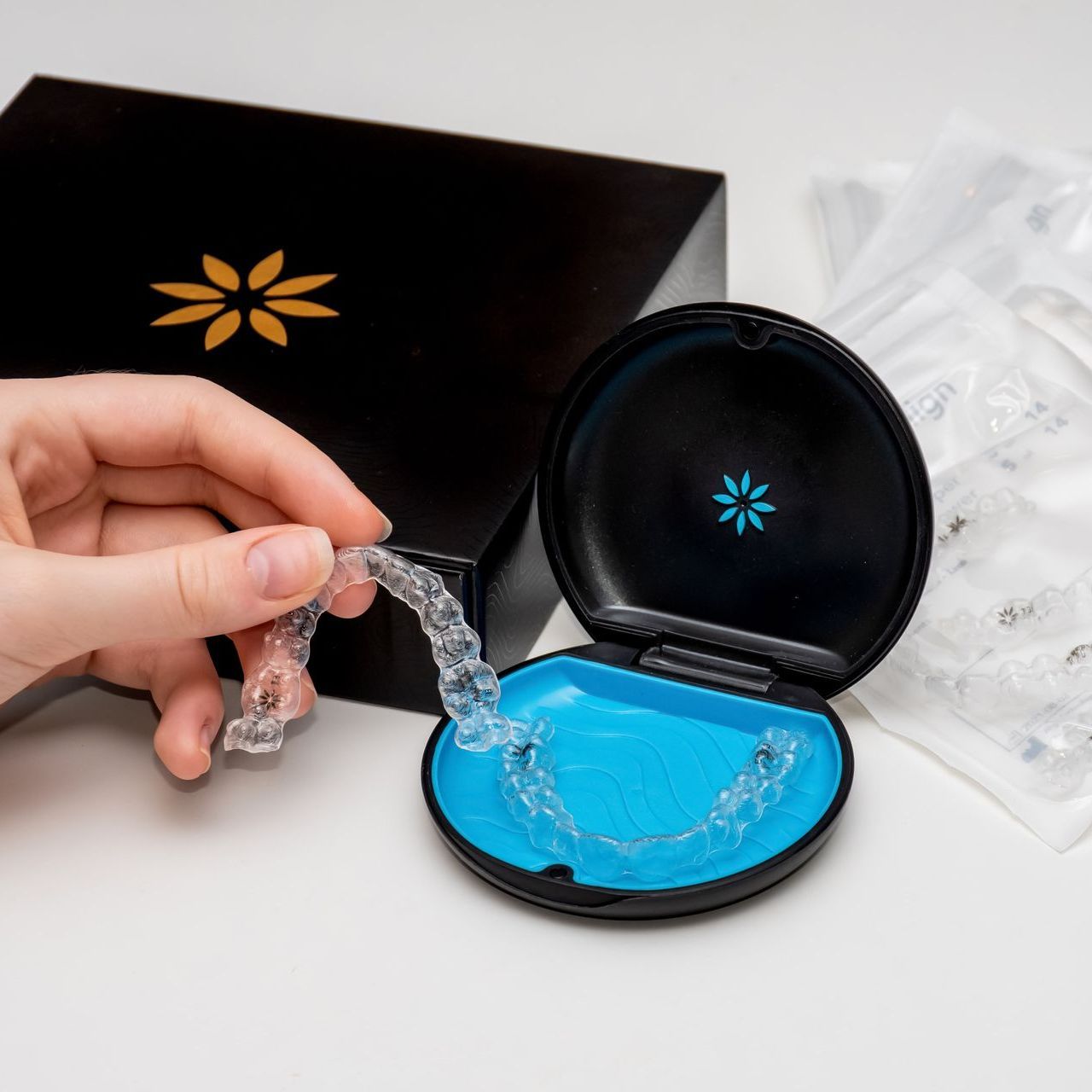 An image showing a hand picking up an Invisalign® clear aligner from its case with an Invisalign® box and aligners in the background