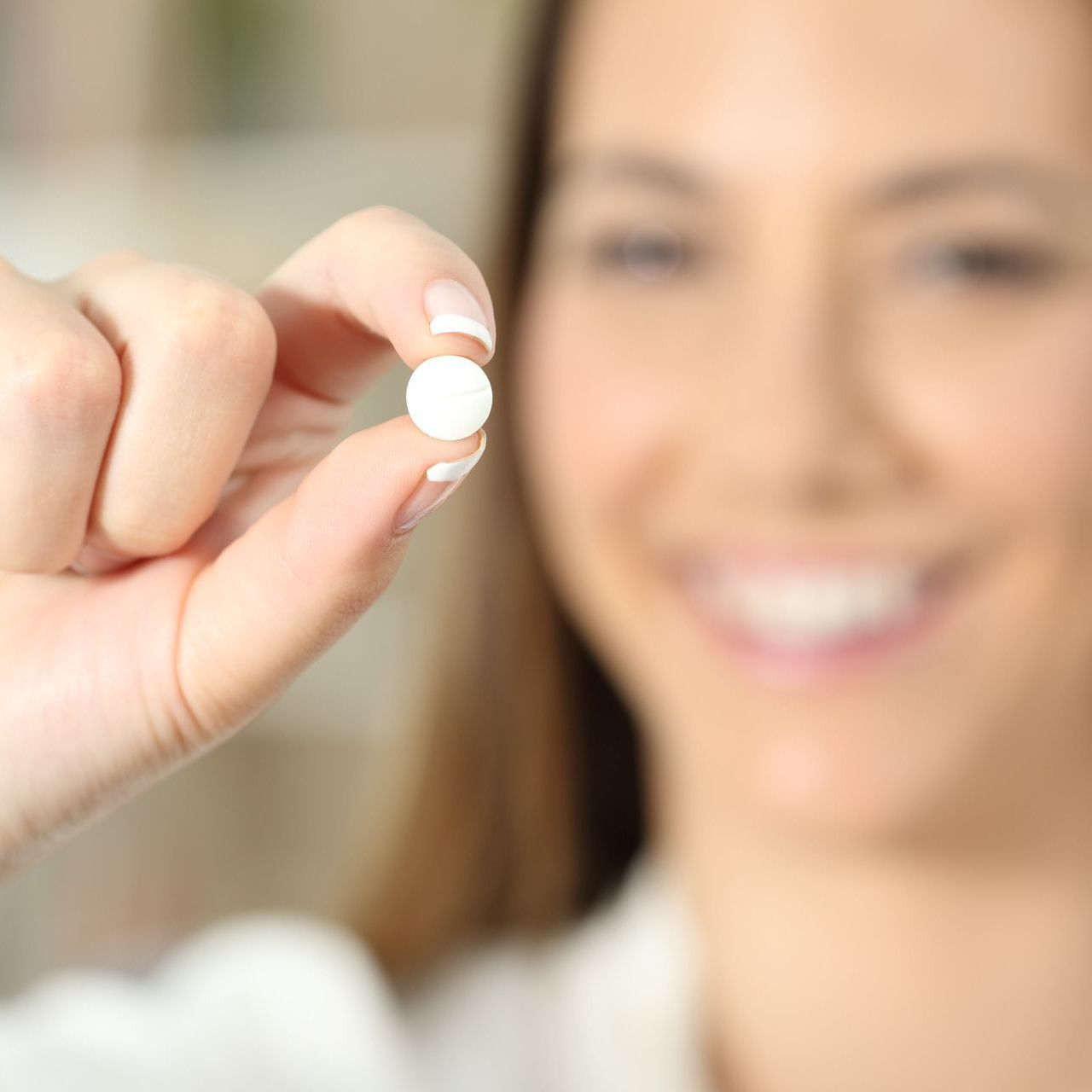 An image of a young woman smiling while holding a pill