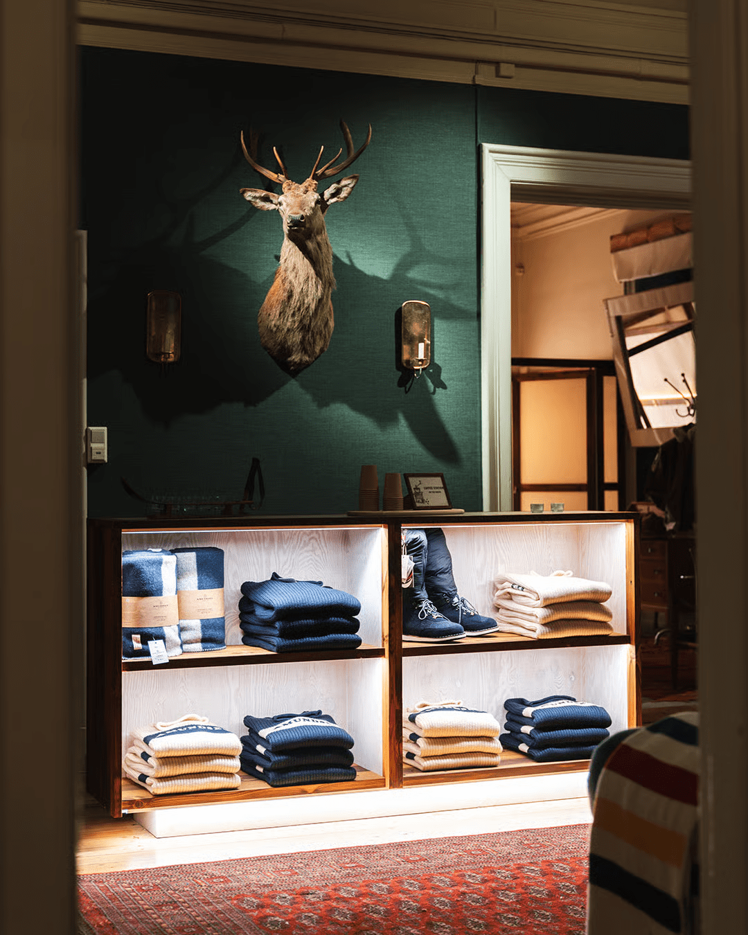 Retail display with deer head mount on dark teal wall, showcasing folded clothing and boots.