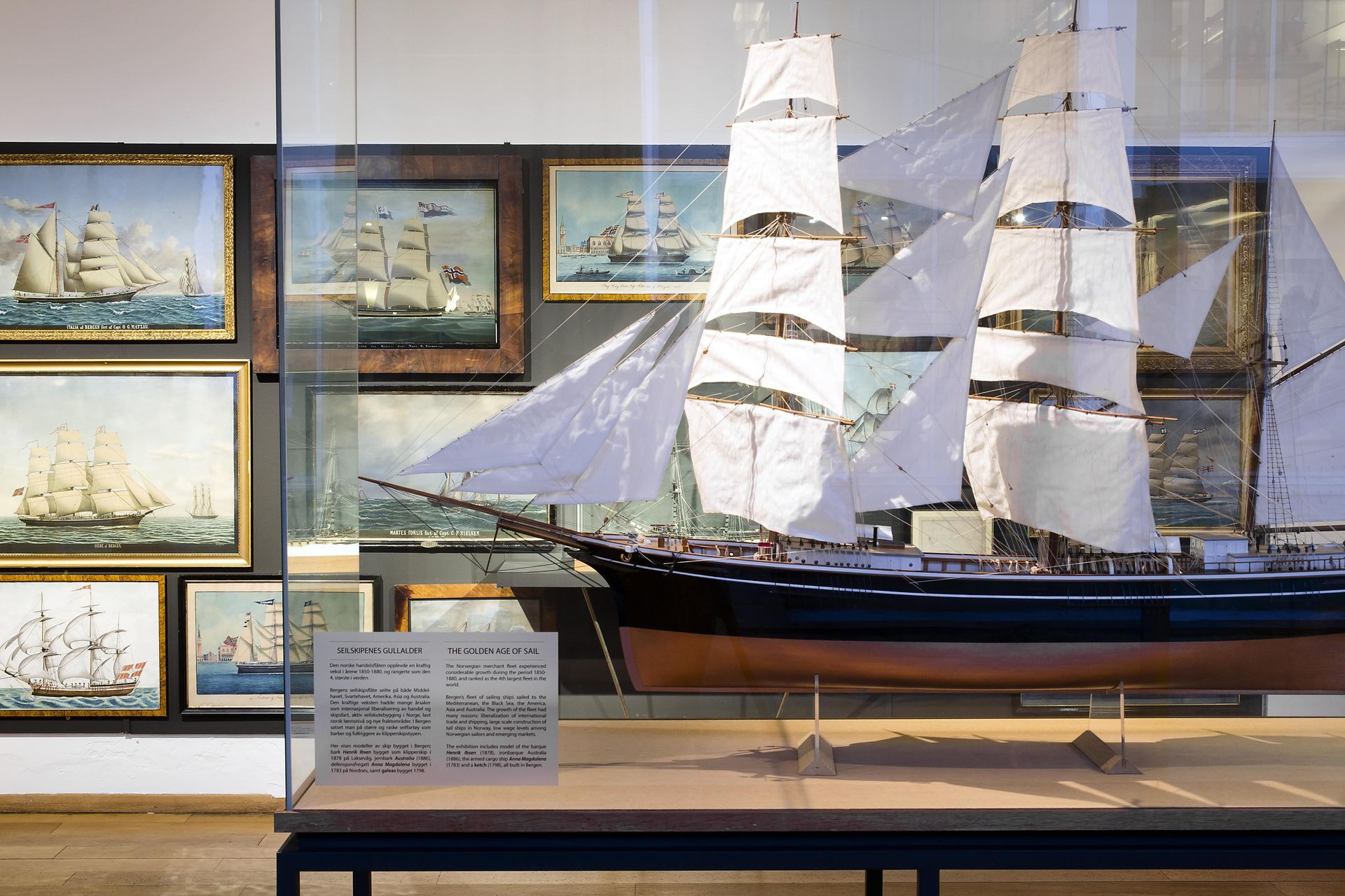 Model ship and maritime paintings displayed in a glass case.