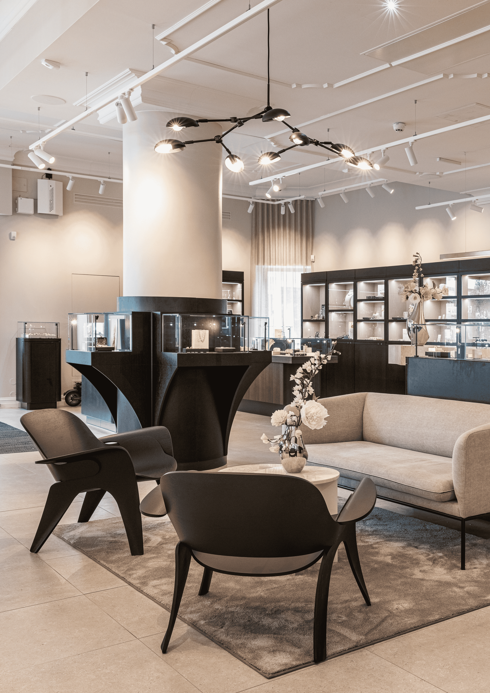 Jewelry store interior with seating area, display cases, and modern chandelier. Neutral tones.