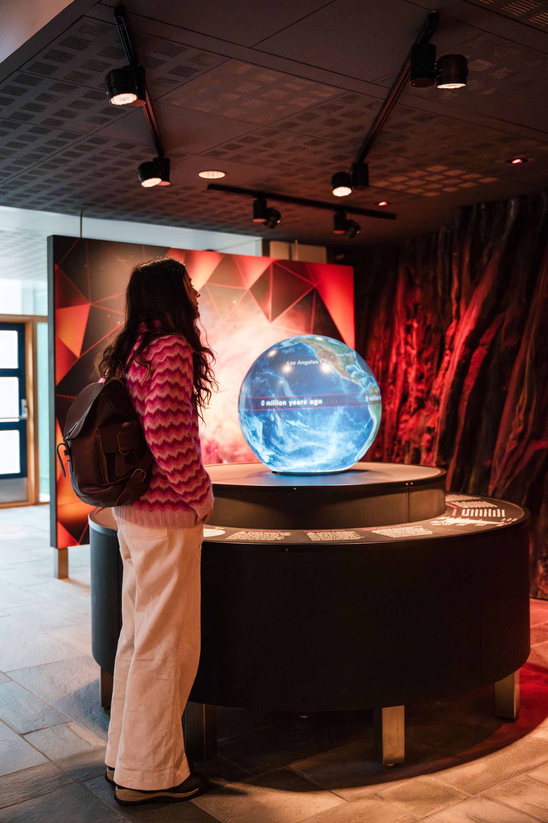 Woman in pink sweater looking at a glowing globe display in a museum.
