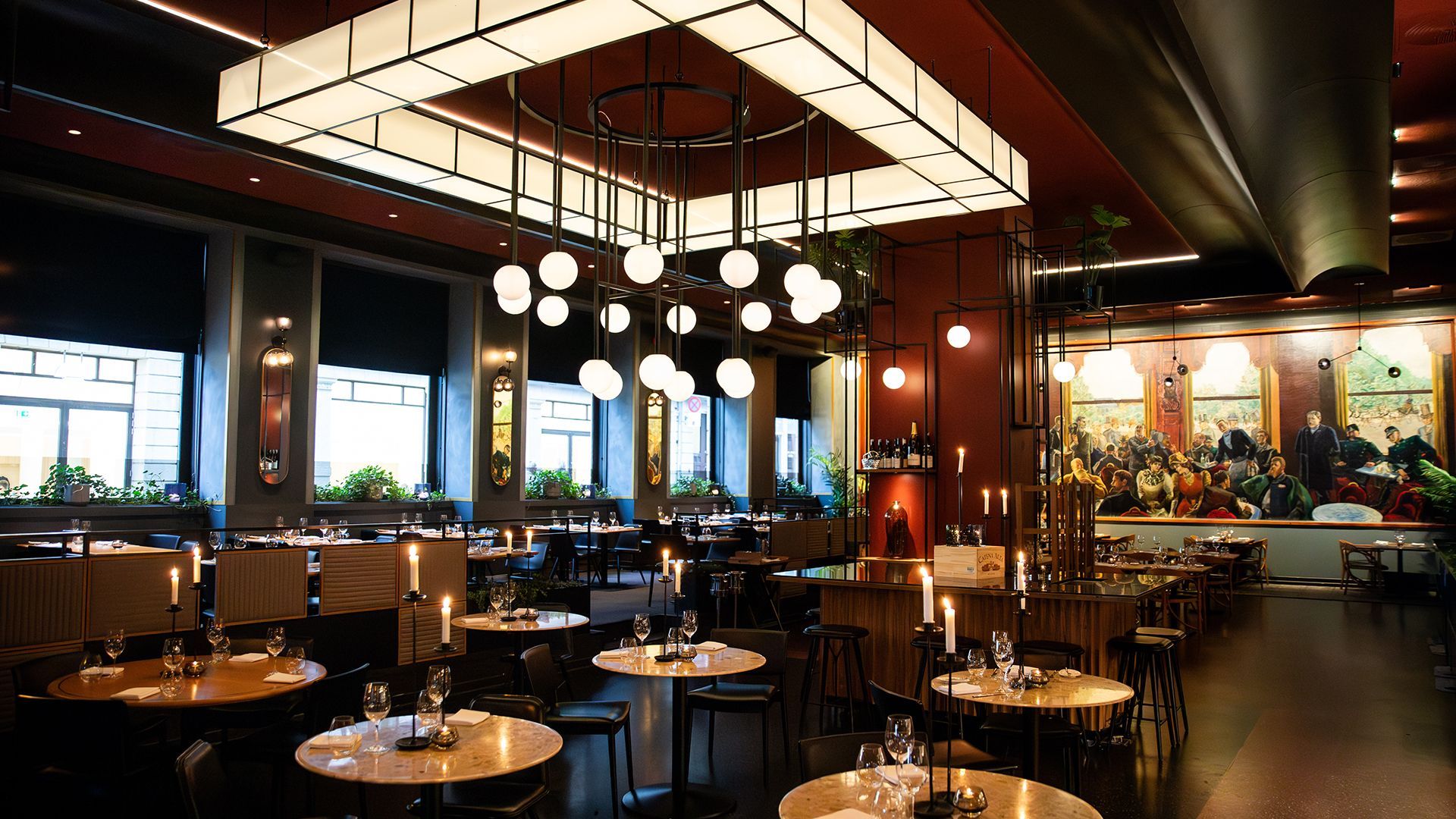 Restaurant interior with round tables, dim lighting, and a large mural.