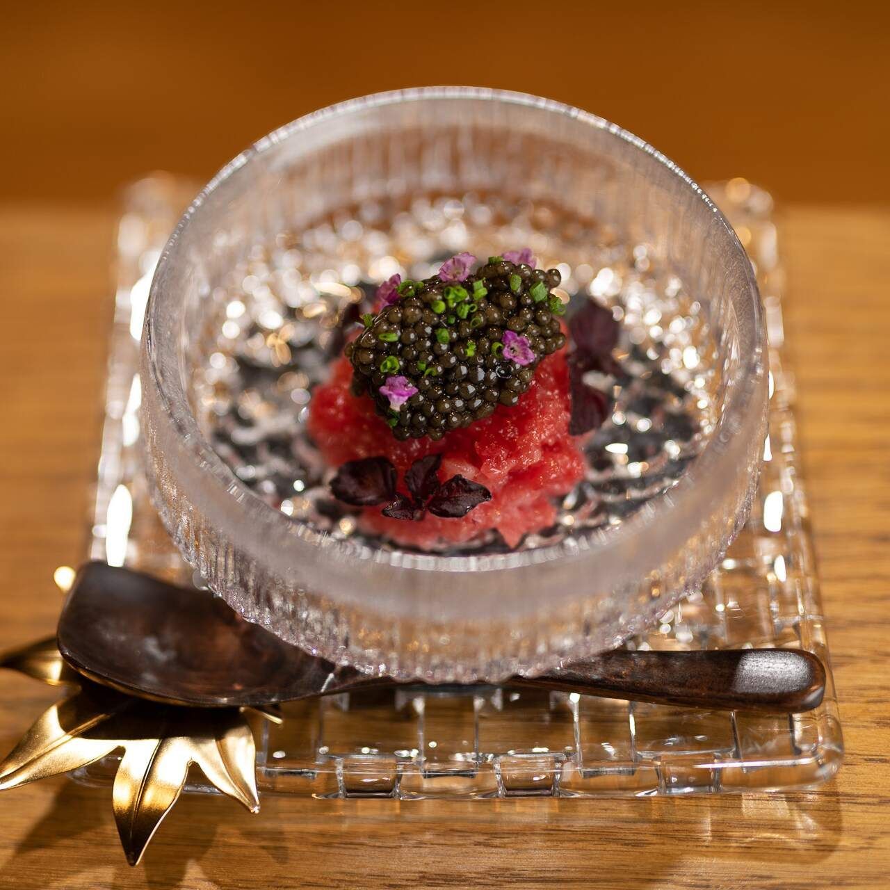Small dish of tuna with caviar and edible flowers, on a glass tray with a spoon.
