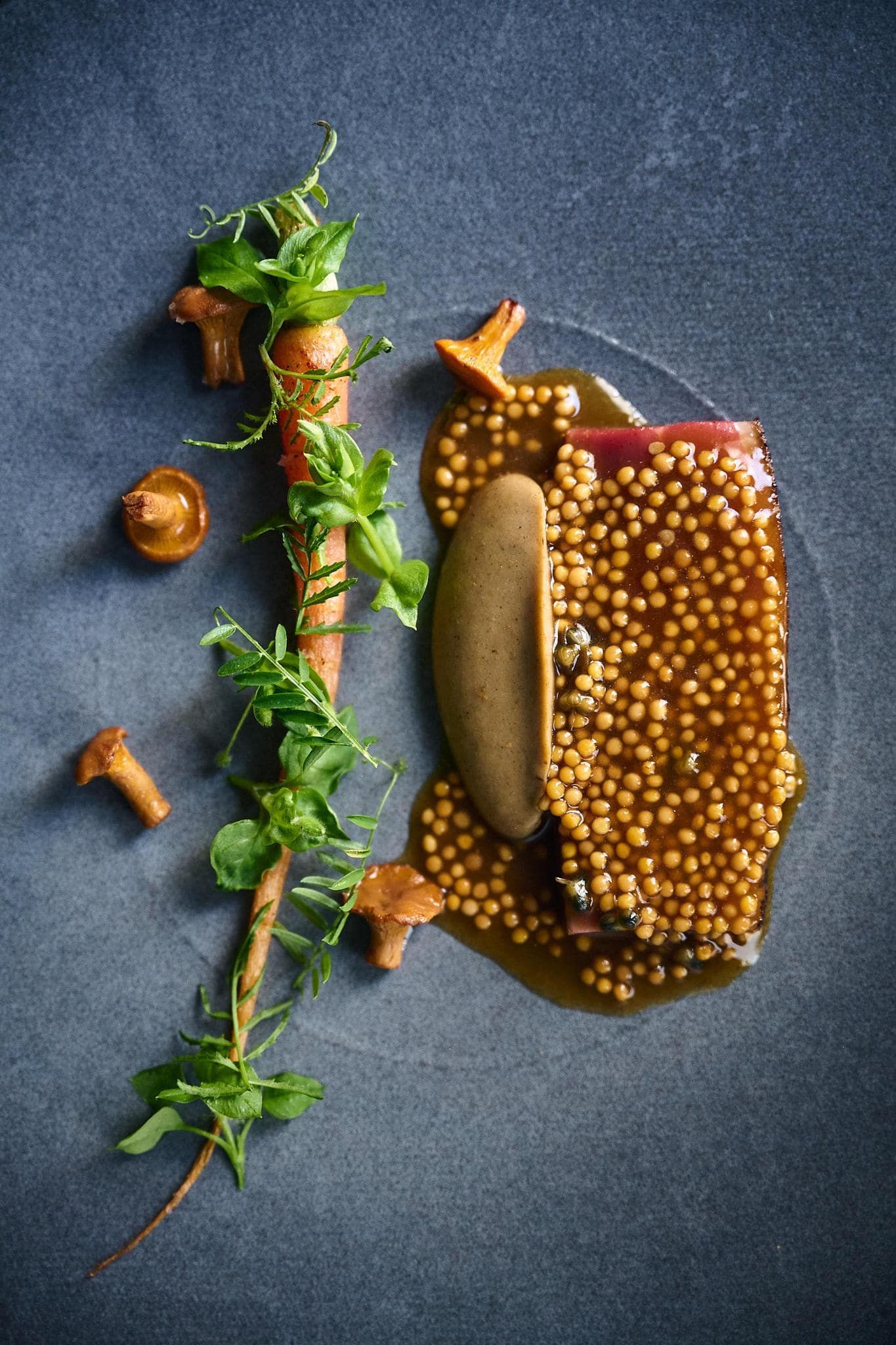 Gourmet dish: Seared meat, mustard seeds, sauce, a root vegetable, and mushrooms on a blue plate.