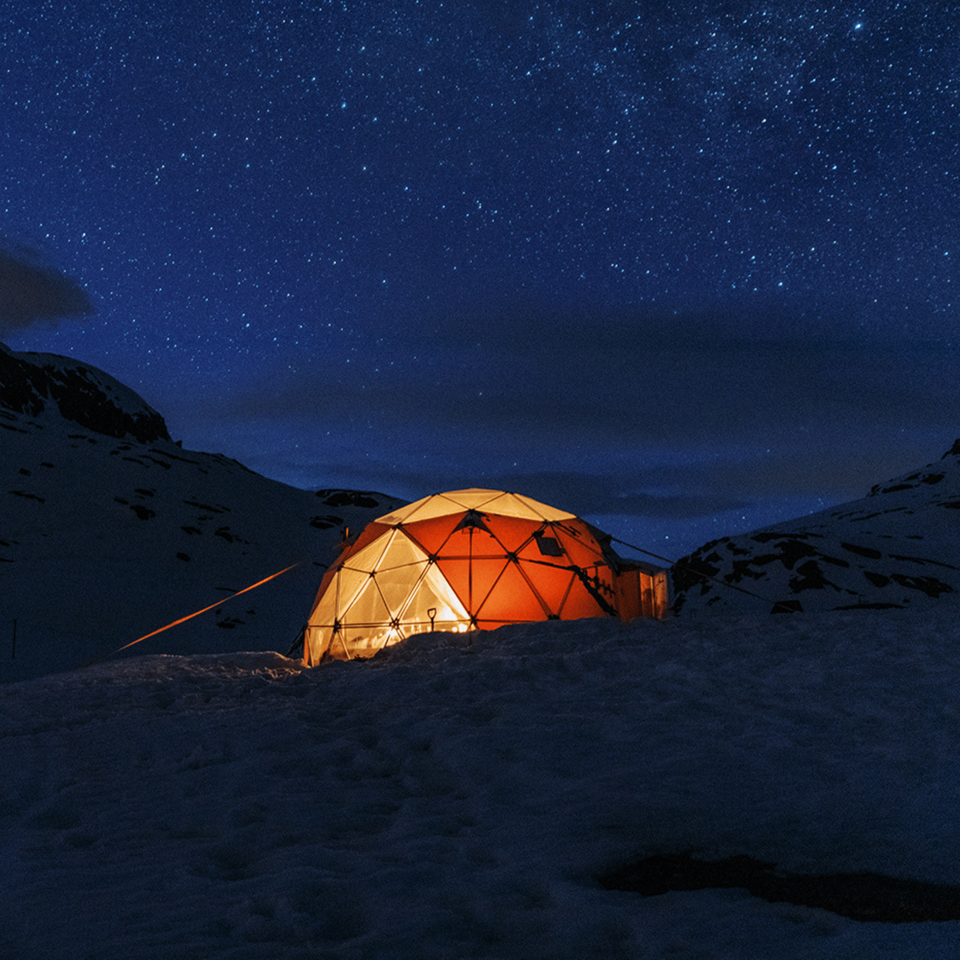Lit dome in snowy landscape under starry night sky.