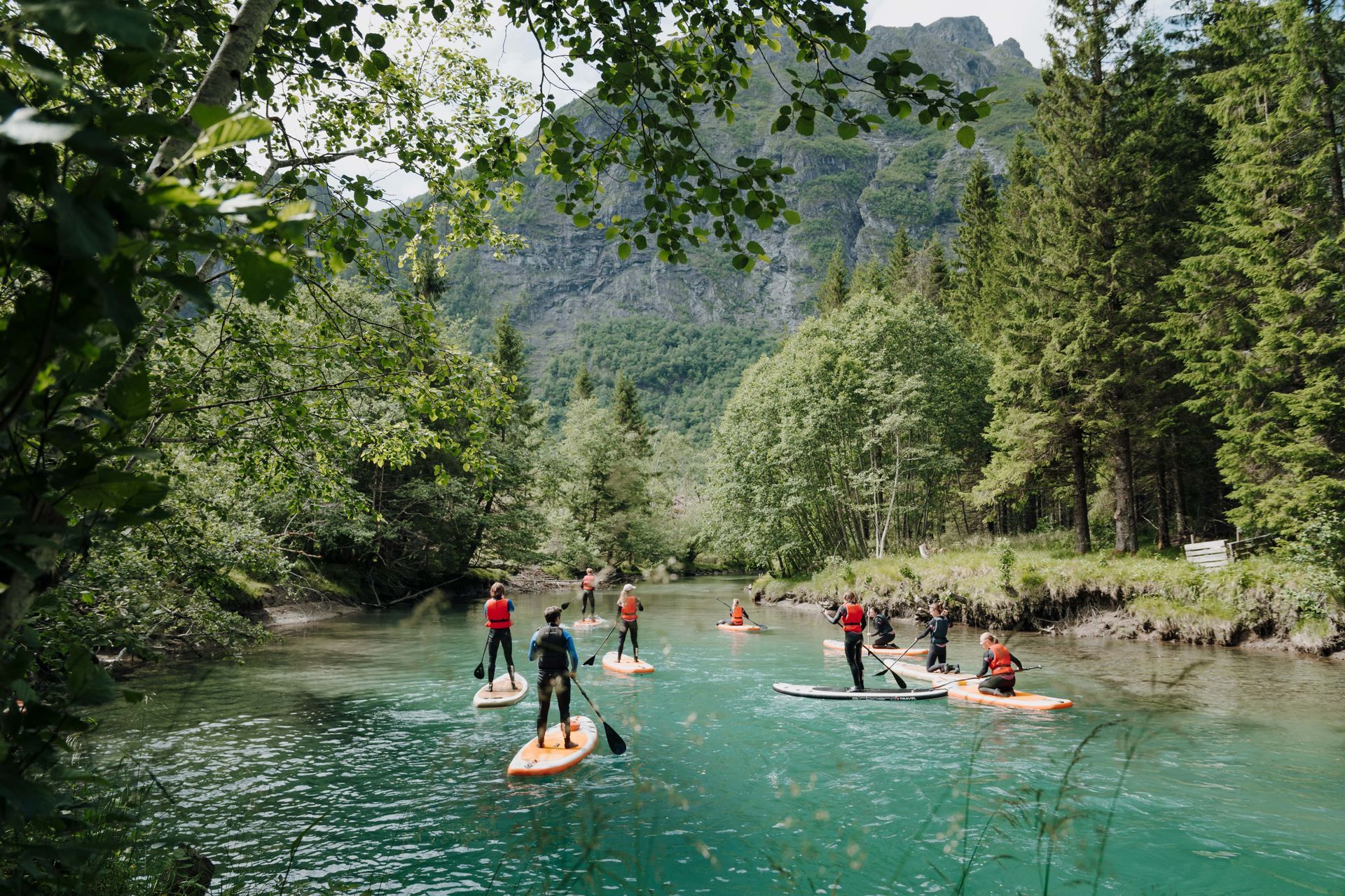 People paddleboarding on a clear, turquoise river surrounded by trees and mountains.