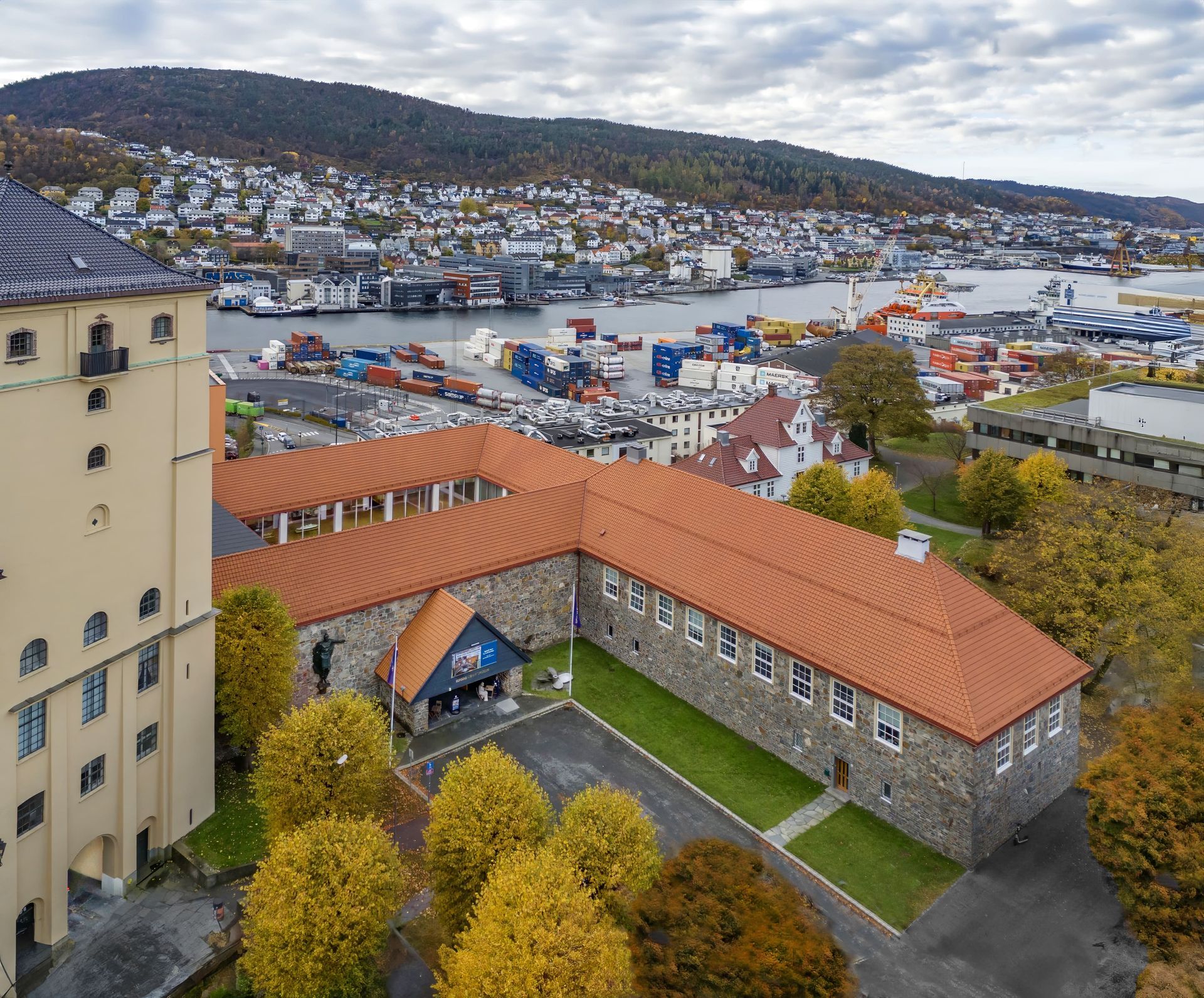 Stone building with red roof, overlooking a city and harbor, fall foliage.