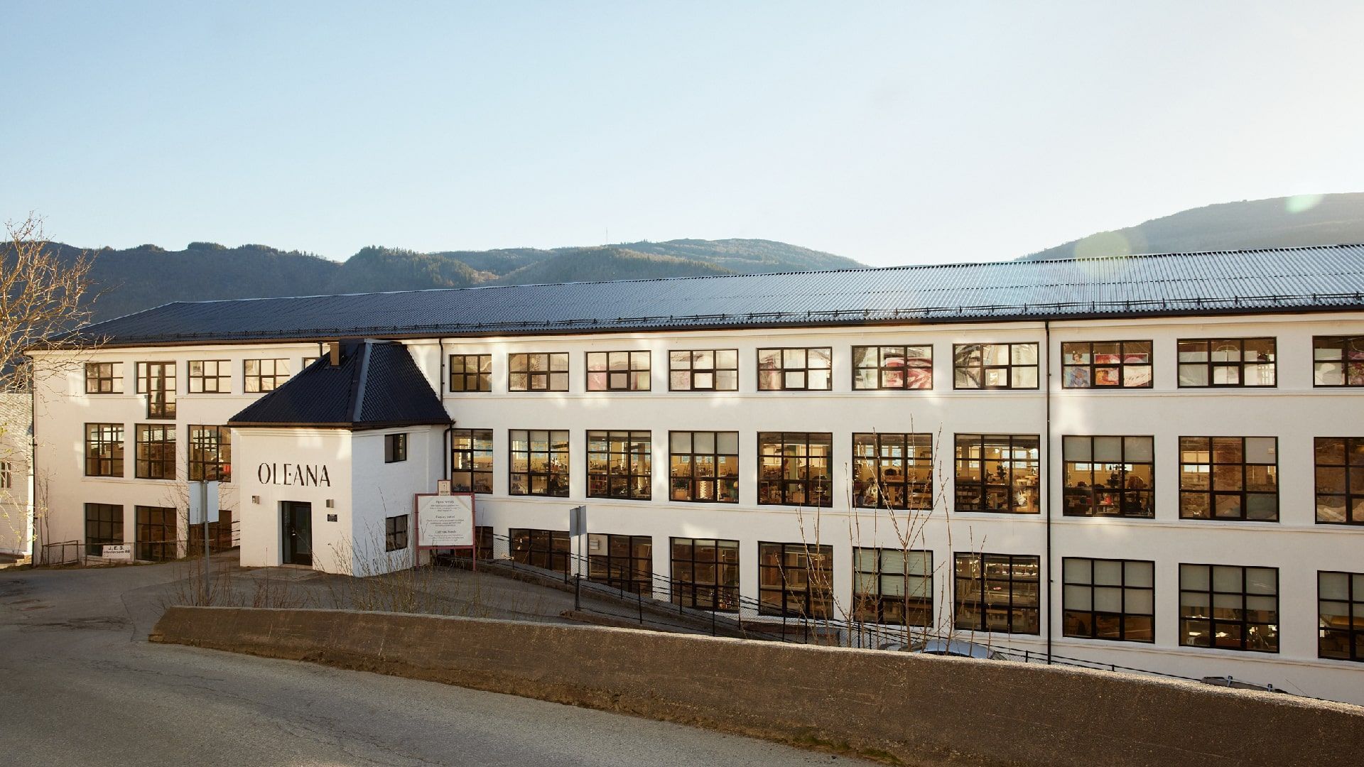 White three-story building with many windows, dark roof, and mountains in background.