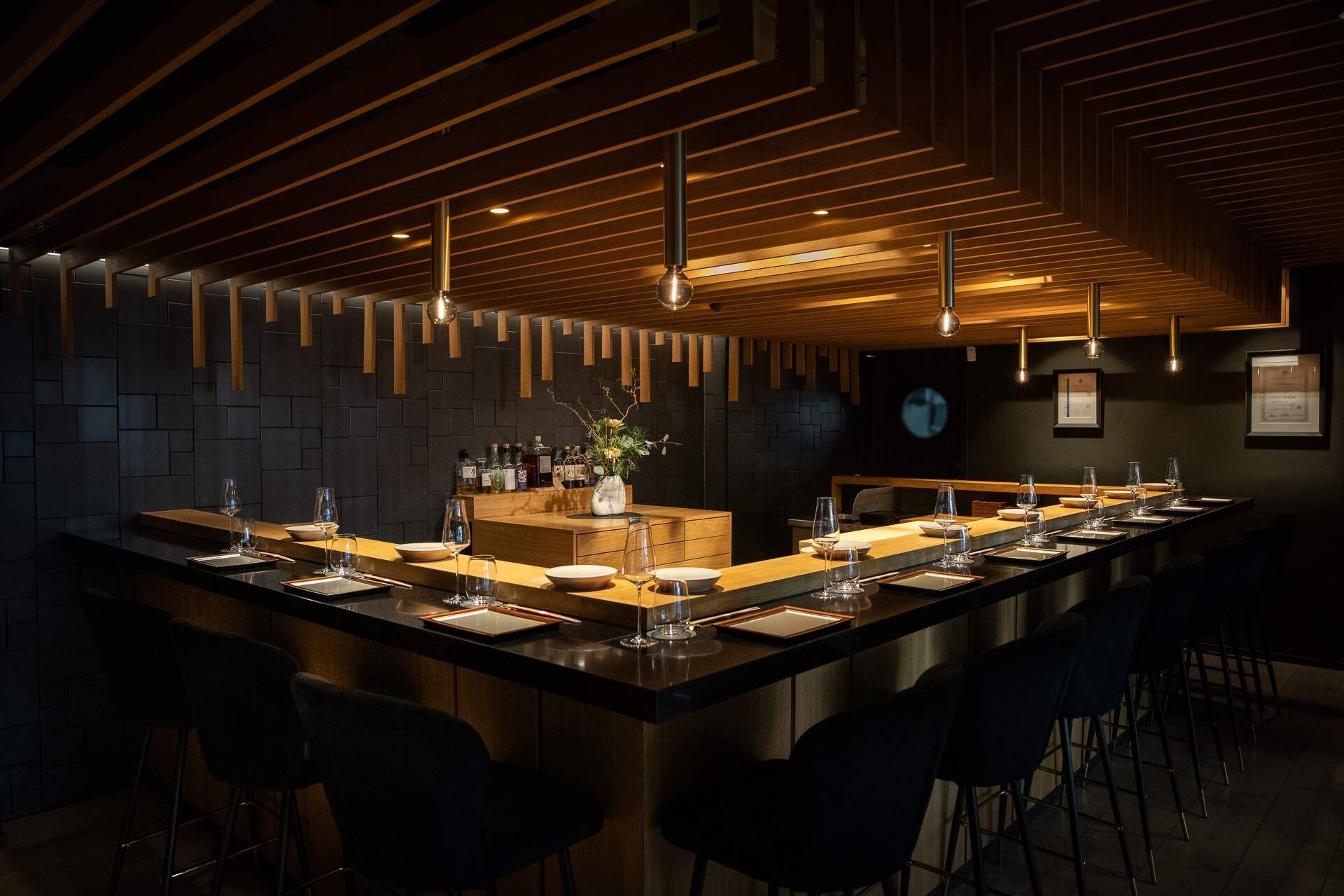 Sushi restaurant interior with a black countertop bar, stools, and a wooden ceiling.