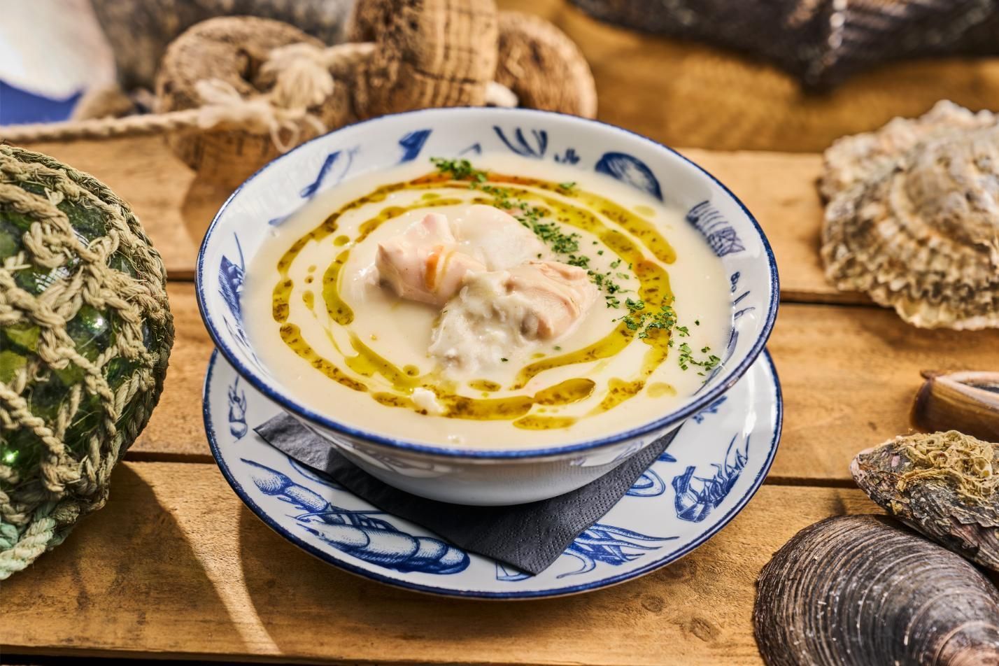 Creamy seafood soup in a blue and white bowl, drizzled with olive oil, on a wooden table.