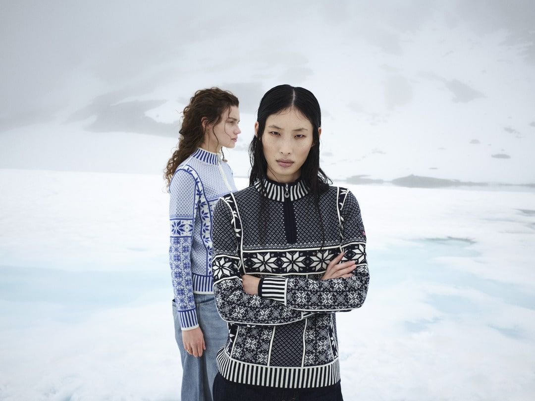 Silhouetted figures on a rocky shore watching a vibrant sunset over water and mountains.