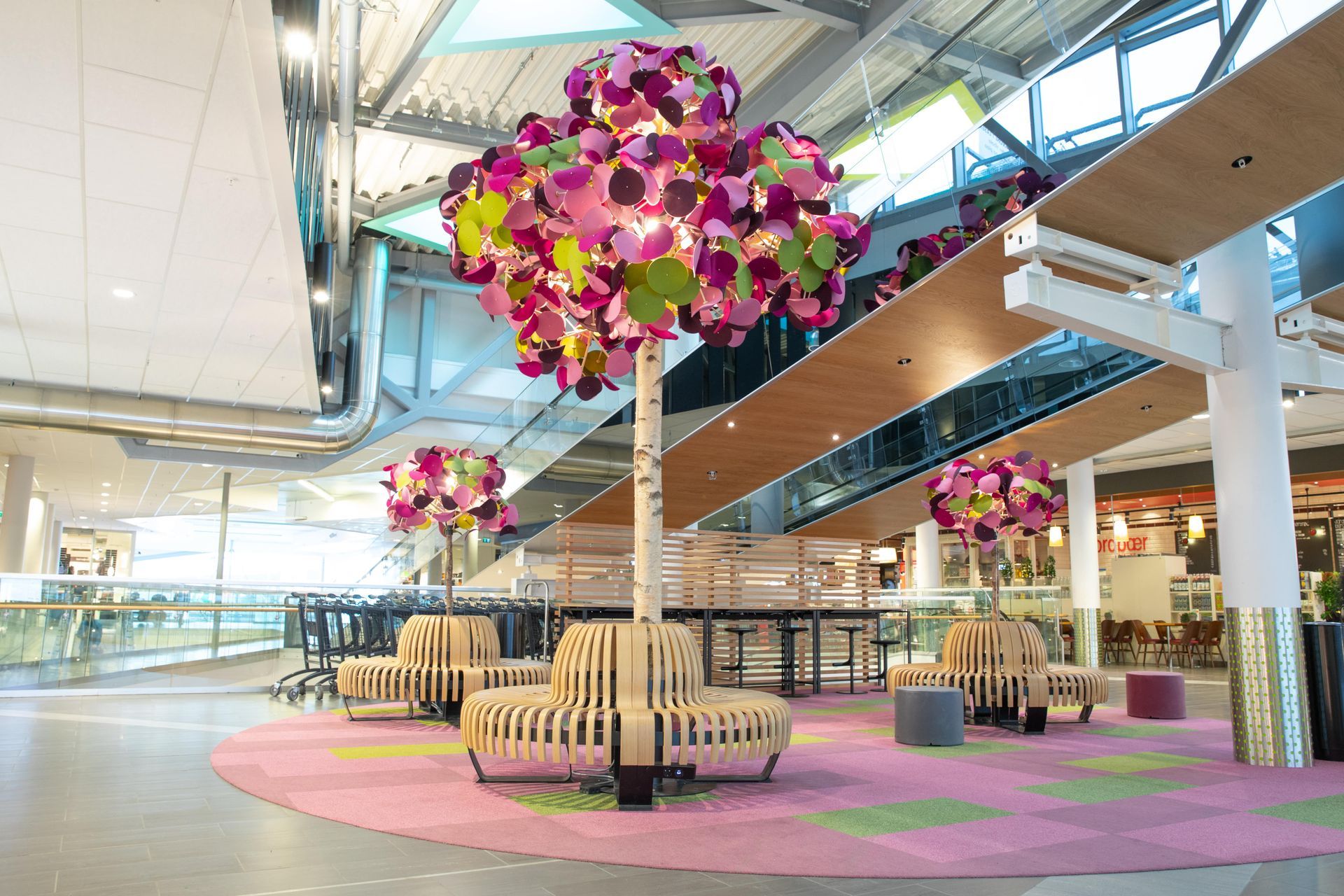 A modern indoor space with decorative tree sculptures, seating, and a pink and green patterned rug.