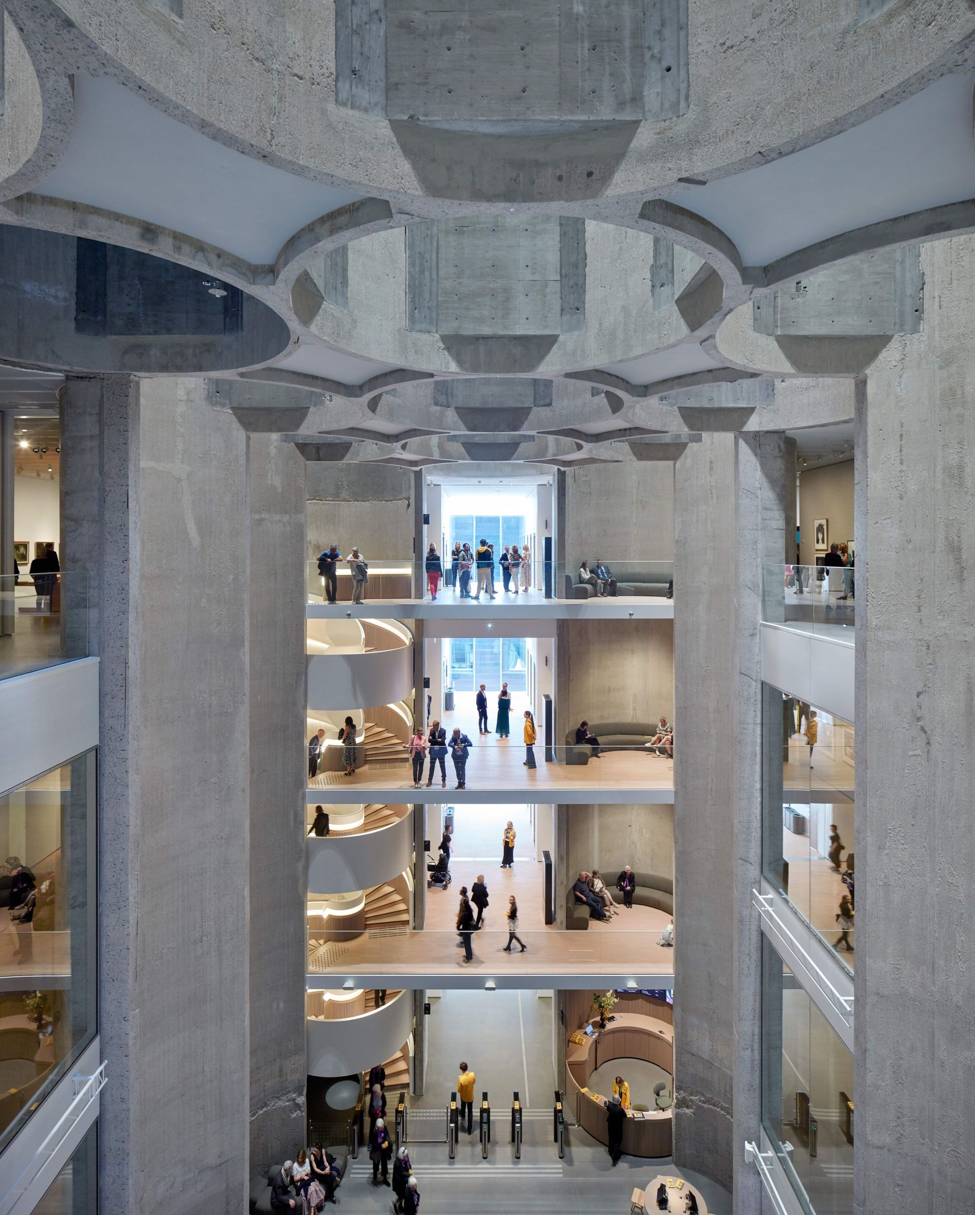Interior view of multi-story concrete building with people on various levels, light-filled with large windows.