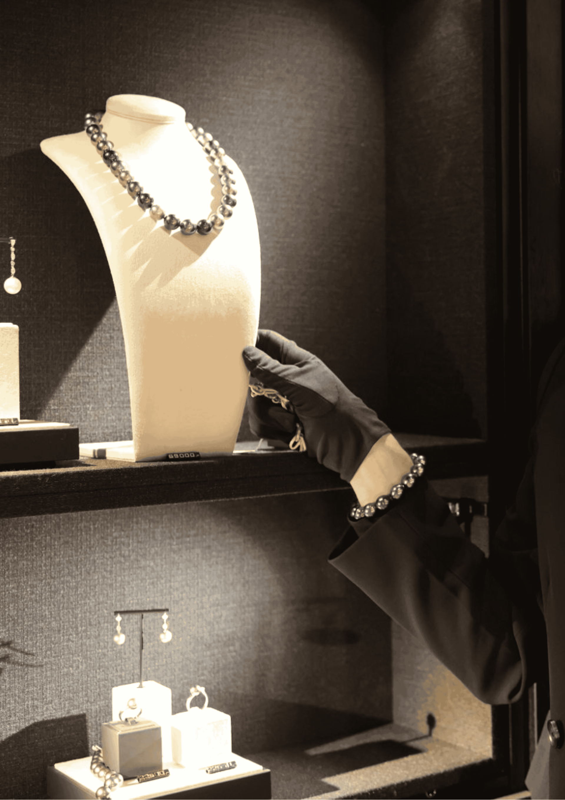 A gloved hand reaches for a necklace on a mannequin inside a jewelry store display.