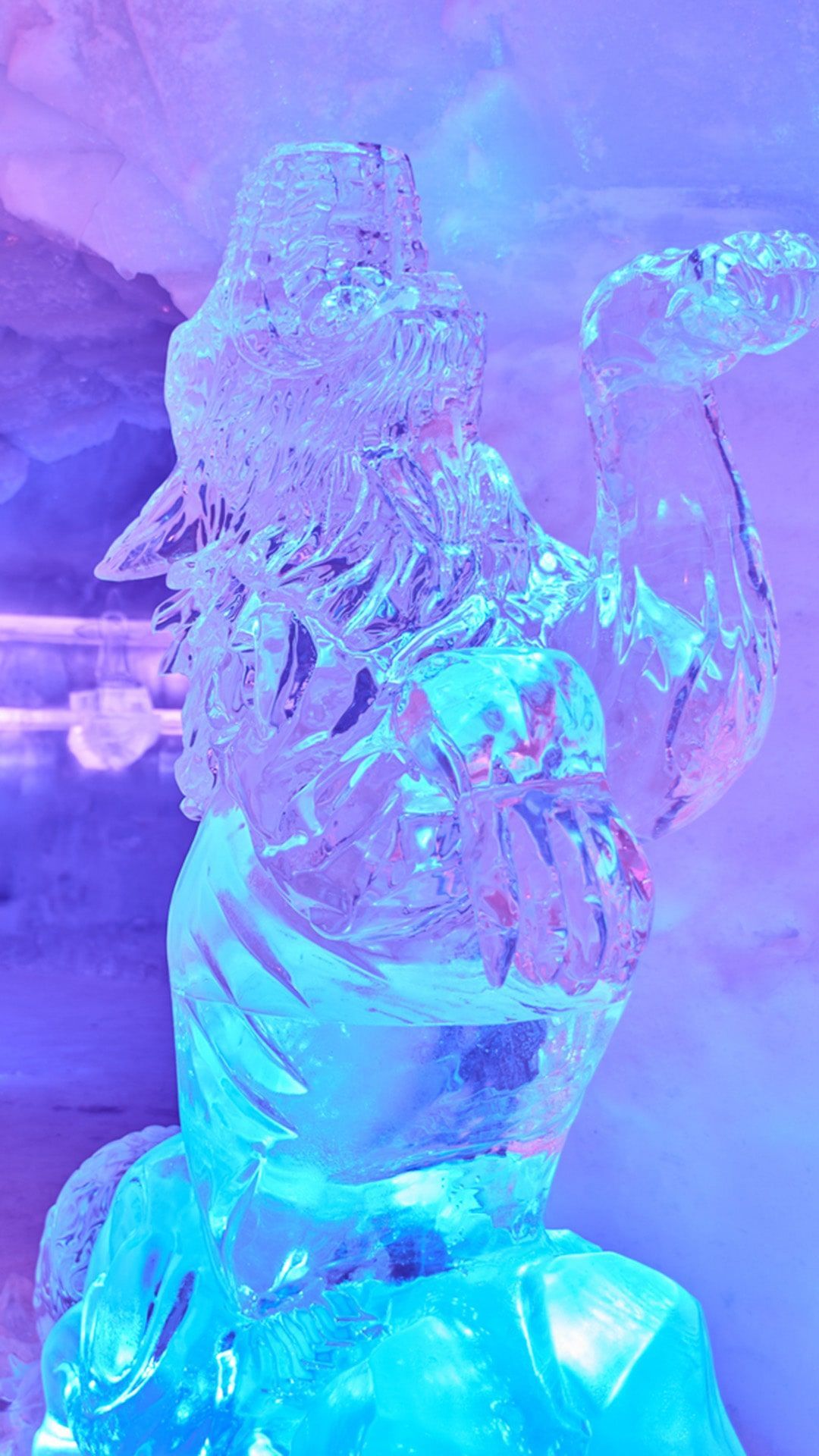 Ice sculpture of a figure wearing a hat and holding a curved object; lit with blue and purple lights.