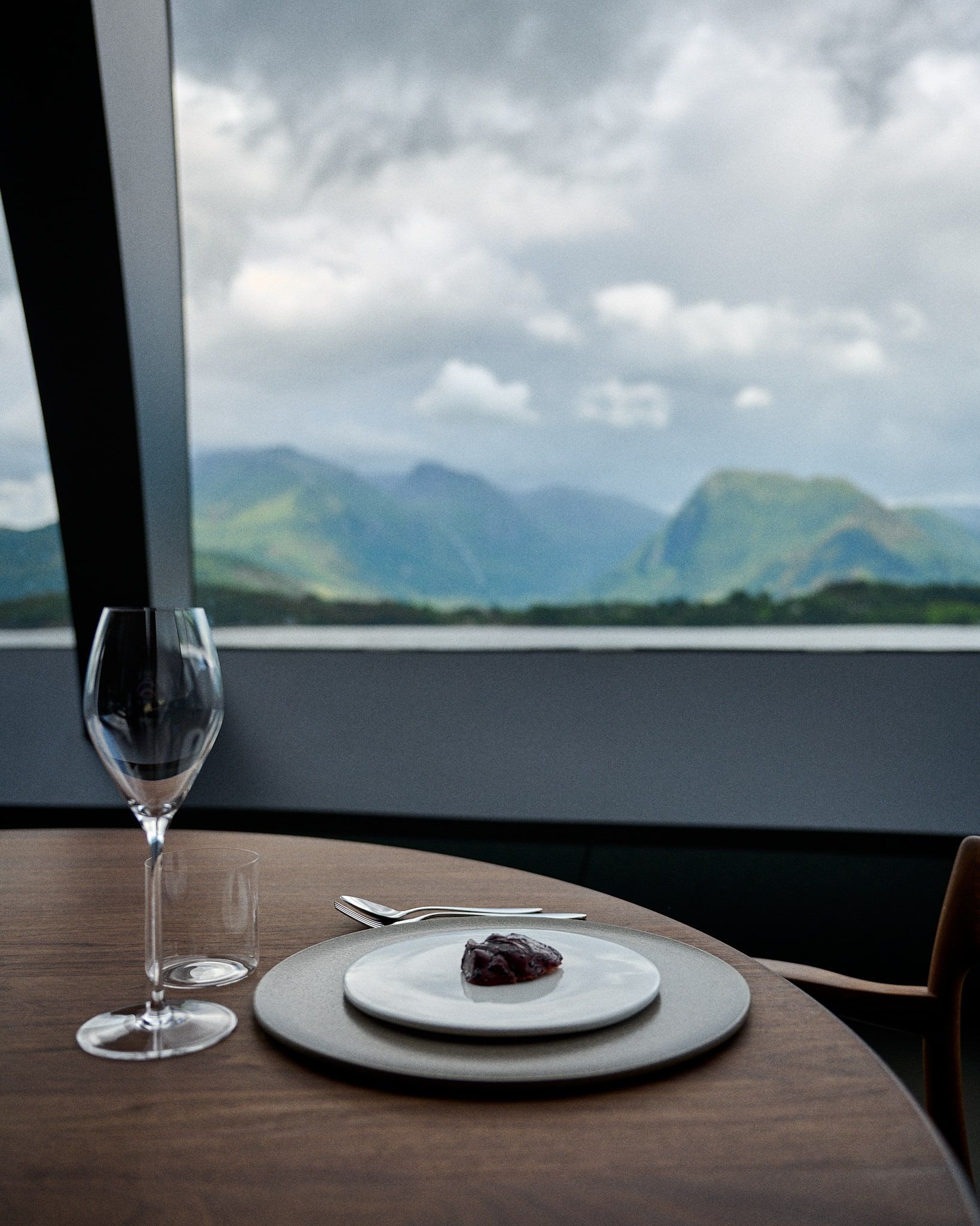 A single plate with food on a table next to a wine glass, with mountains and water in the background.
