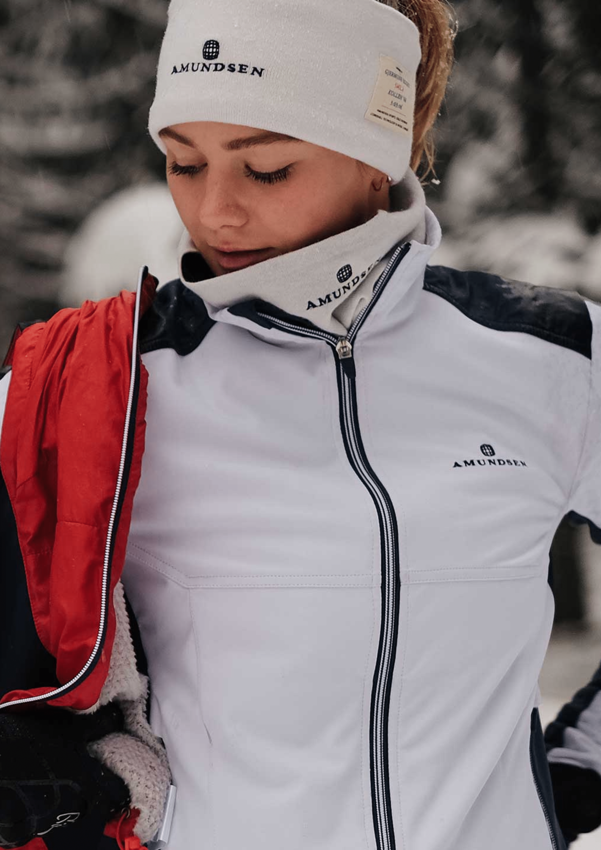 Woman in white jacket and headband, outdoors in the snow, adjusting her jacket.