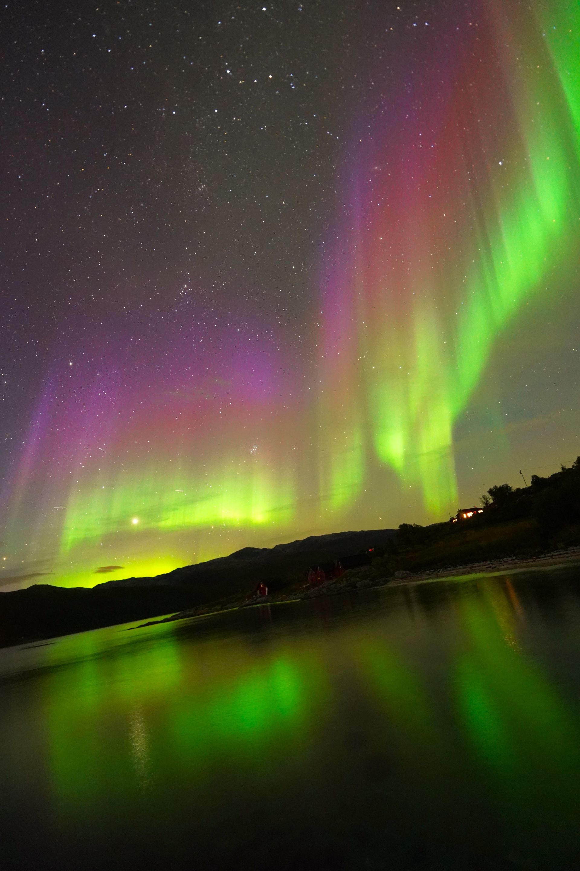 Aurora borealis with green and purple lights reflecting on water.