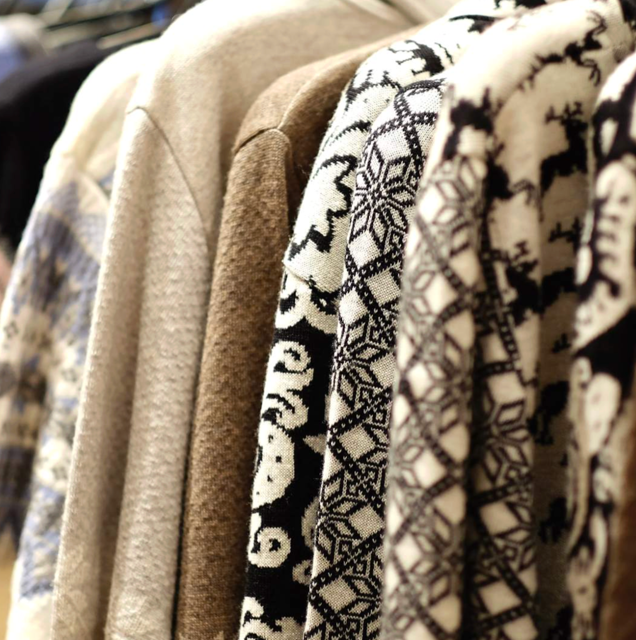 Sweaters of various colors and patterns hang on a rack.