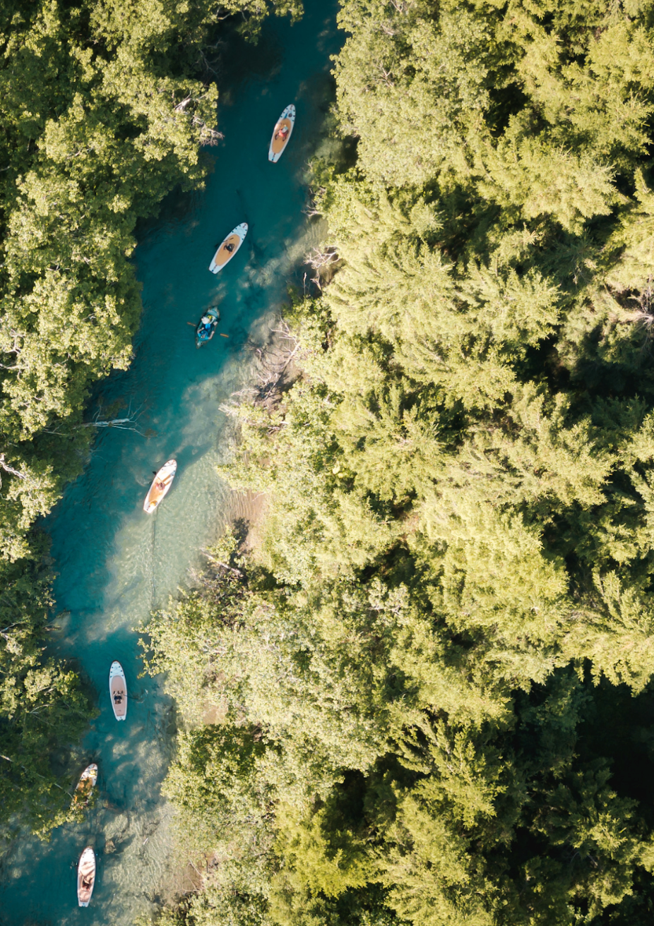 Aerial view of a river surrounded by trees, with paddleboards and people enjoying the water.