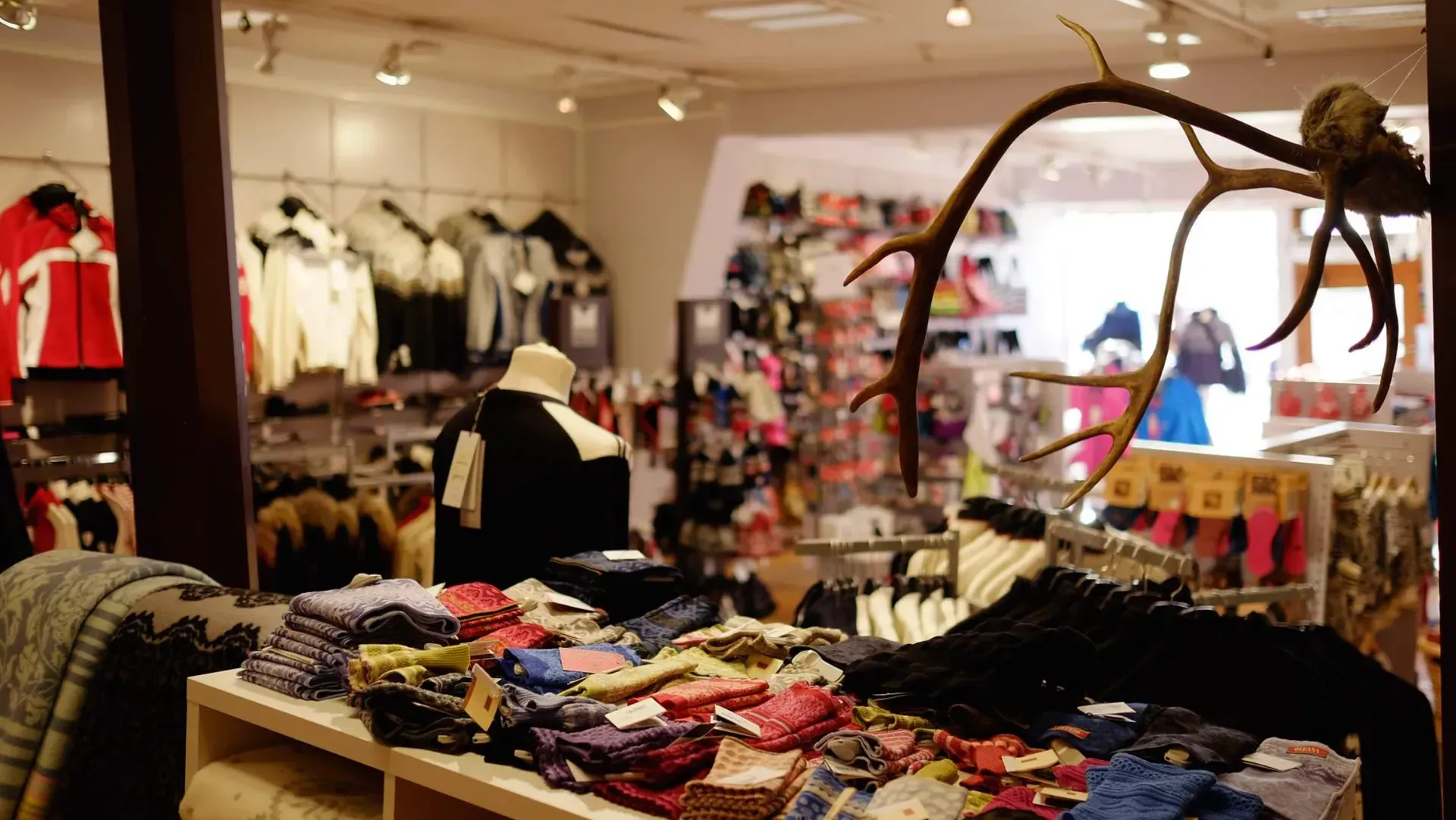 Clothing store interior, jackets and accessories on display, antlers in foreground.