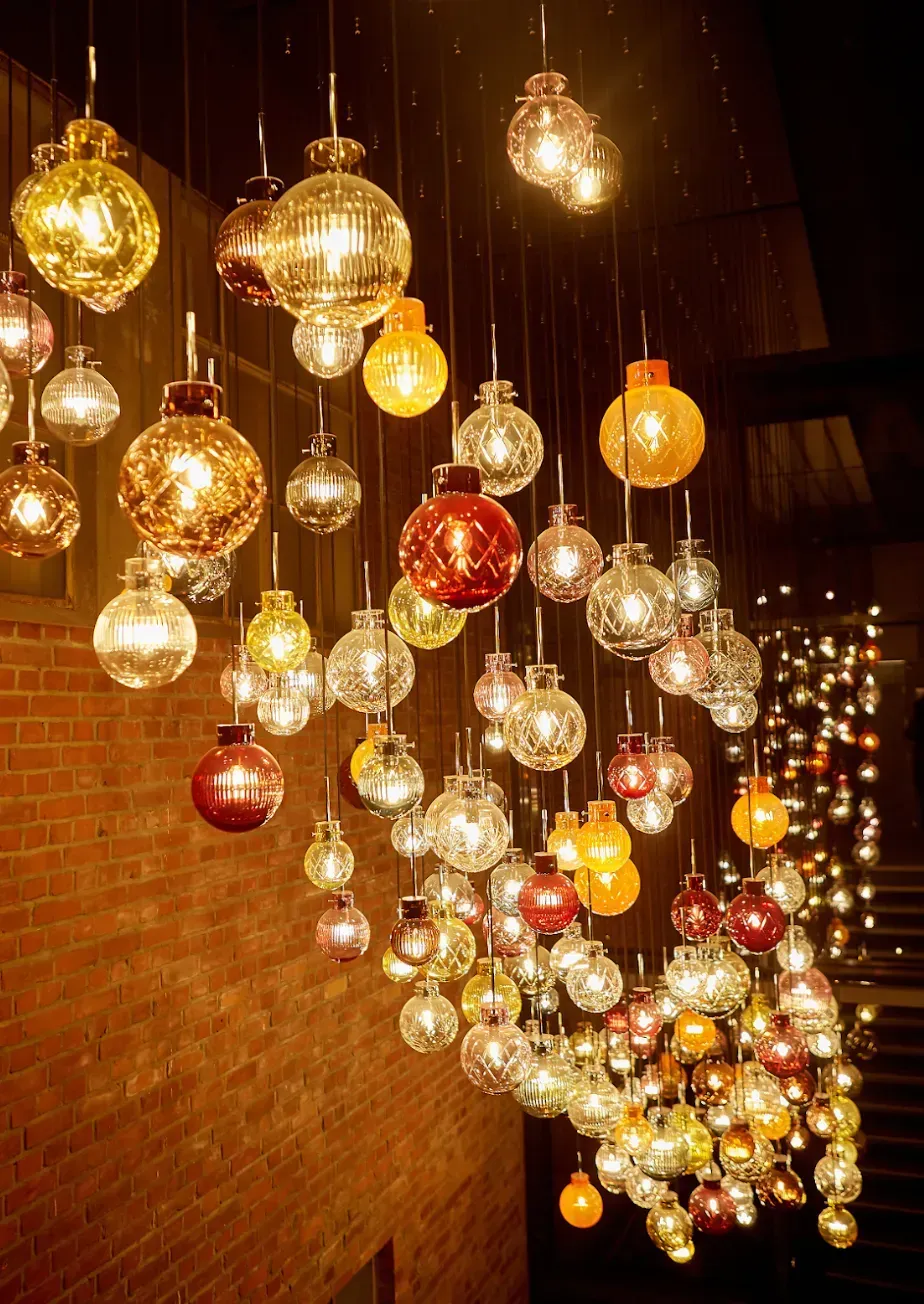 String of decorative glass pendant lights, varying colors, suspended from a high ceiling.