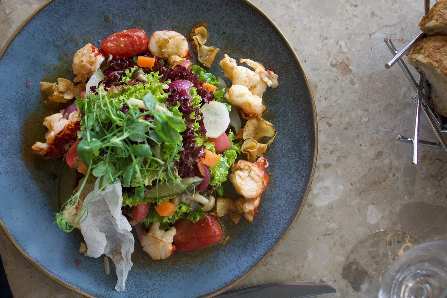 Lobster salad with tomatoes, greens, and chips on a blue plate. Bread in a holder visible.