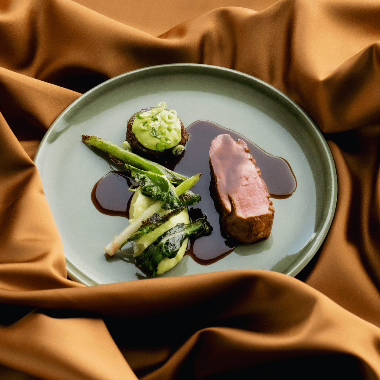 Plate of meat with dark sauce, vegetables, and a mashed side, on a green plate.