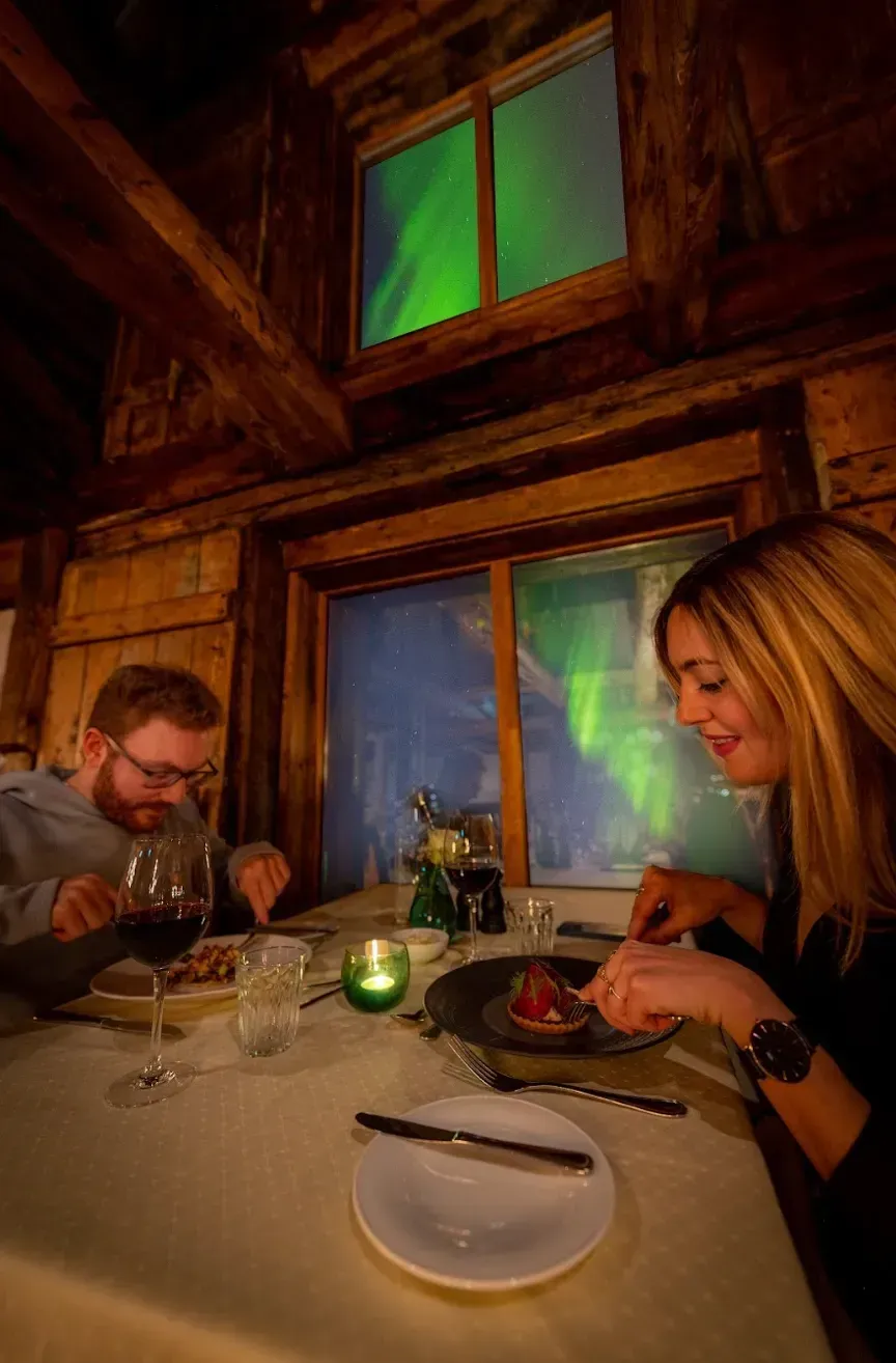 Couple dining indoors, looking at their food with a green aurora visible through the window.