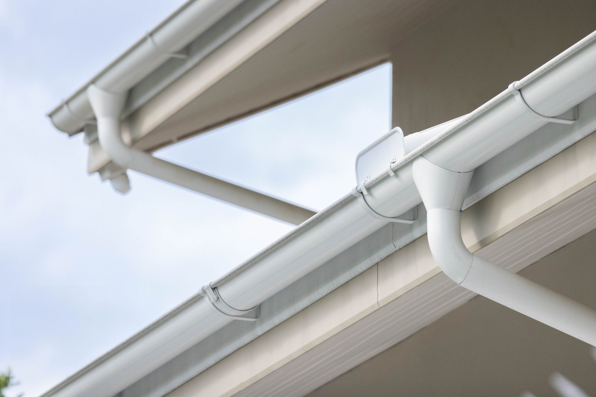 A close-up of white rain gutters and downspouts on a house roof with a clear blue sky.