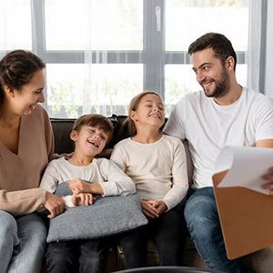 A family sitting together on a couch, smiling and laughing as they look at papers on a clipboard.
